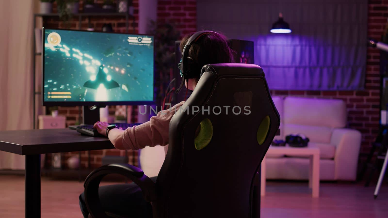 Over shoulder view of gamer girl relaxing playing rpg action game on professional pc setup while talking using headset. Woman streaming on internet fast paced space shooter simulation gameplay.