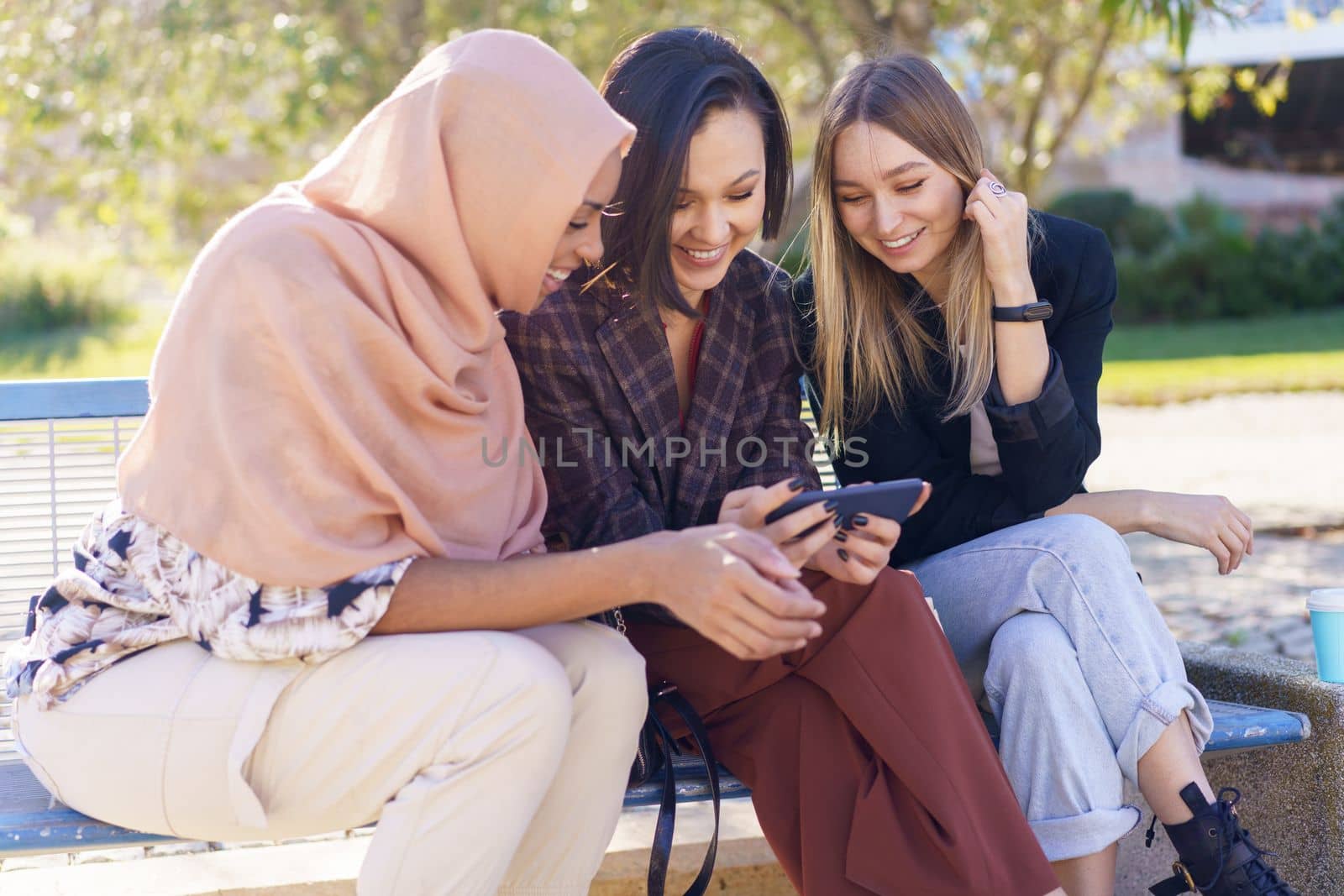 Smiling young diverse women watching video on smartphone in park by javiindy
