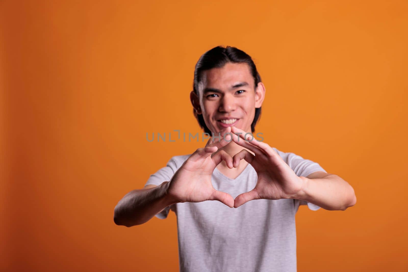 Young happy asian man feeling love, showing heart shape with fingers, focus on hands. Smiling cheerful teenager making appreciation sign, romance symbol, looking at camera