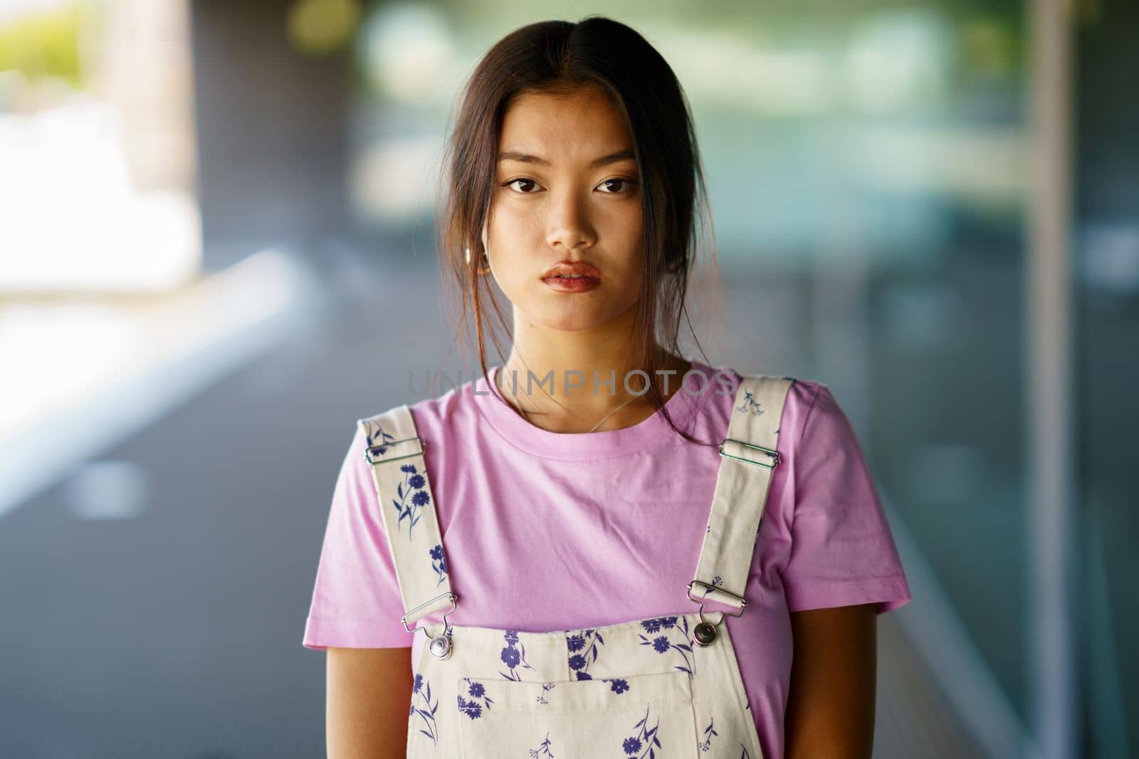 Young Chinese woman looking at camera with serious expression in a modern office building. Female wearing casual clothes.