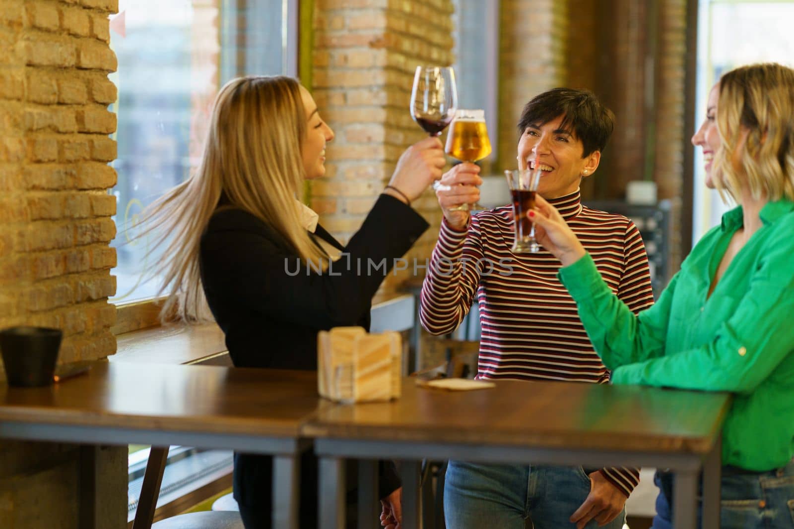 Glad girlfriends clinking glasses near bar window by javiindy