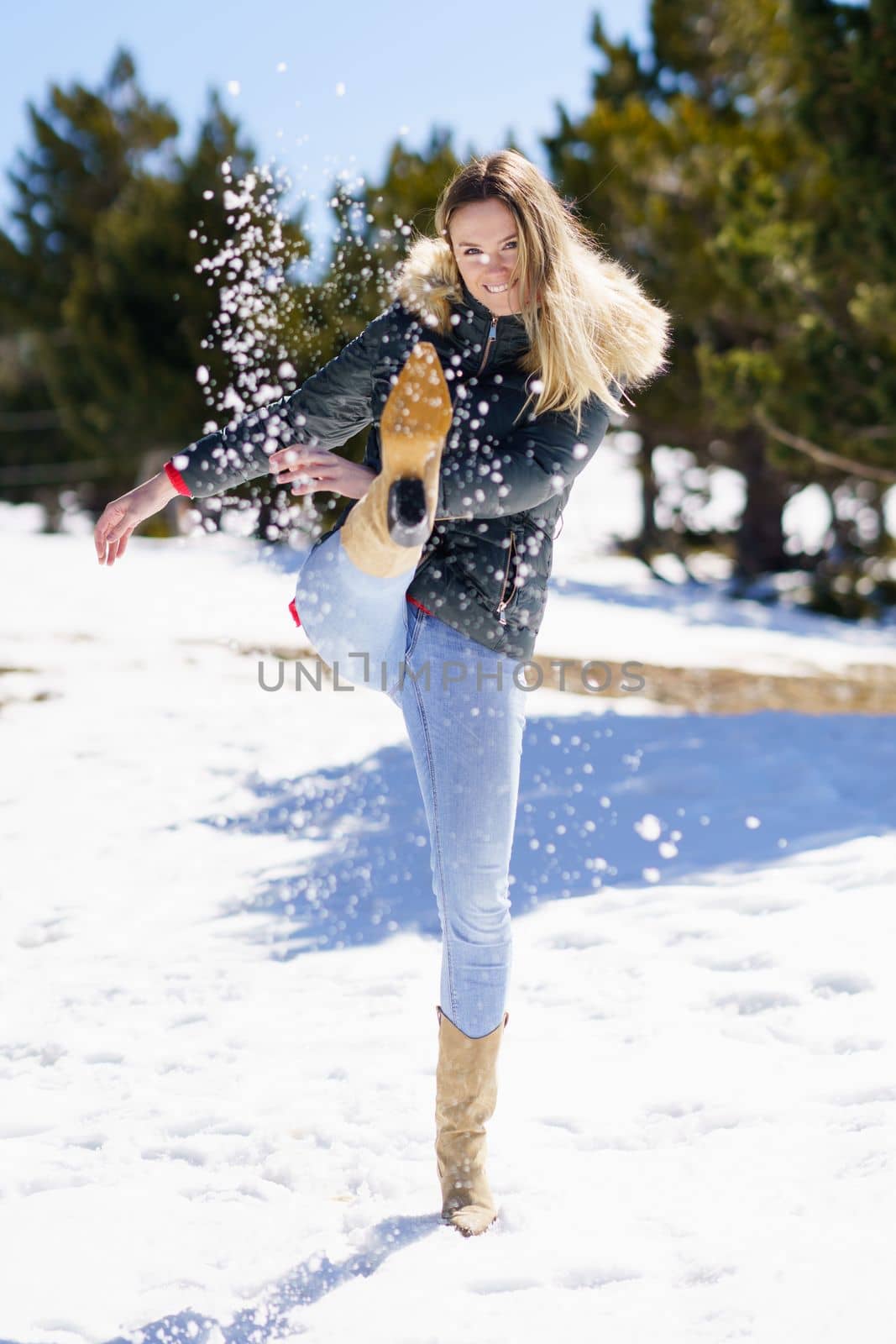 Young happy woman kicking snow in a snow-covered forest in the mountains by javiindy