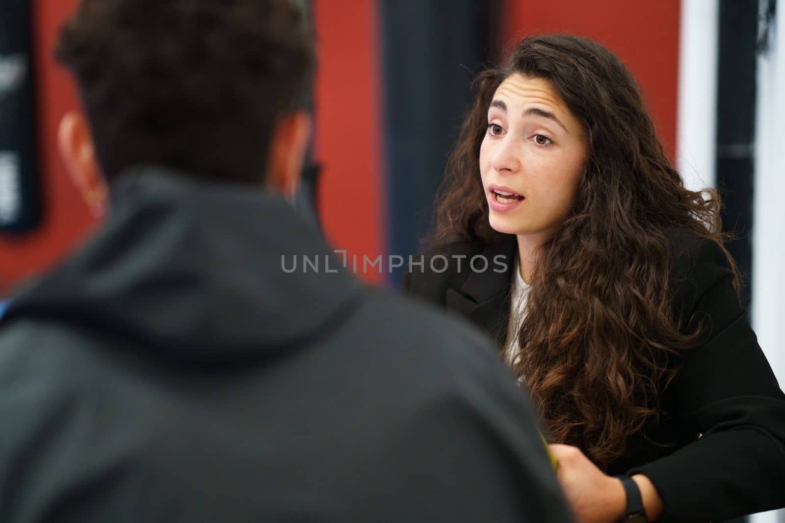 Young brunette talking with sportsman to improve performance during motivational therapy session in gym