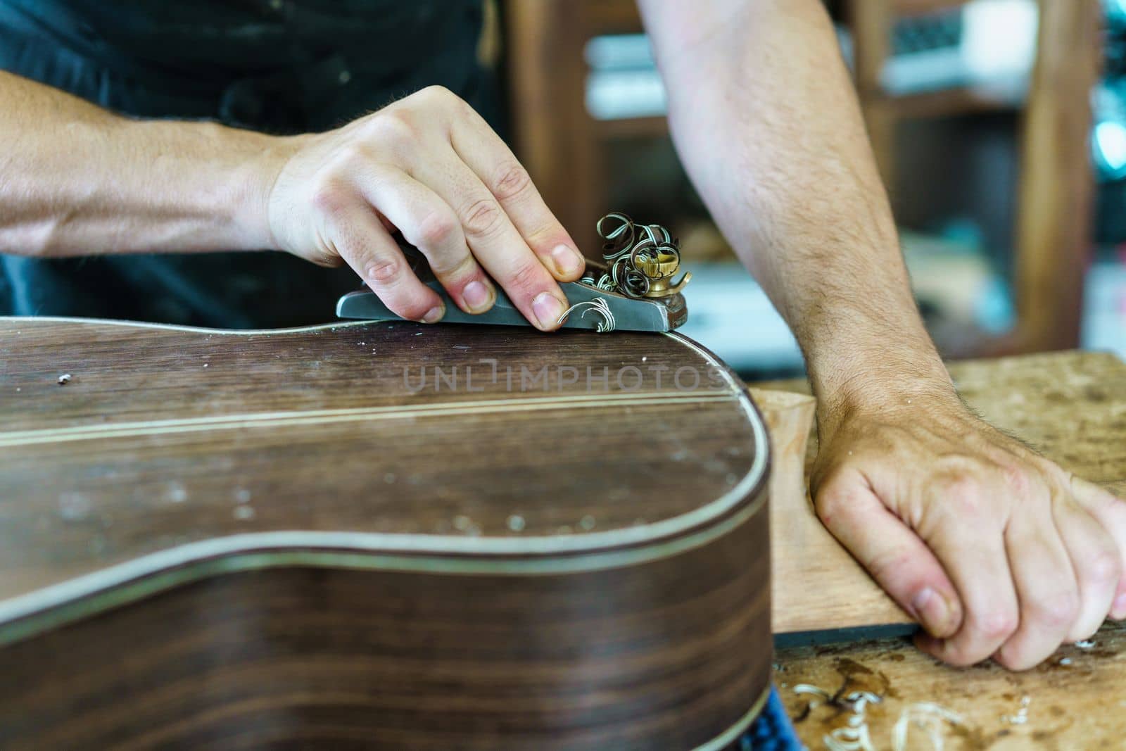 Crop craftsman using plane to shave traditional Spanish flamenco guitar on workbench in workshop