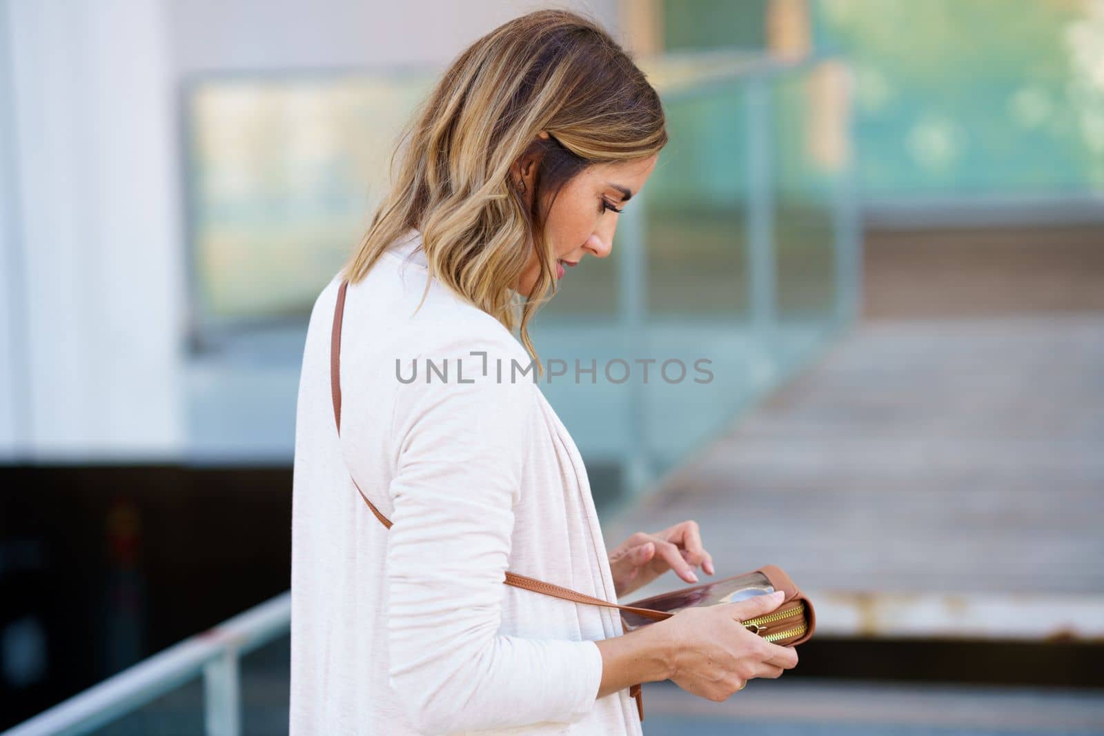 Middle-aged woman using her smartphone through a handbag with space to touch the touch screen. Caucasian female on urban background.