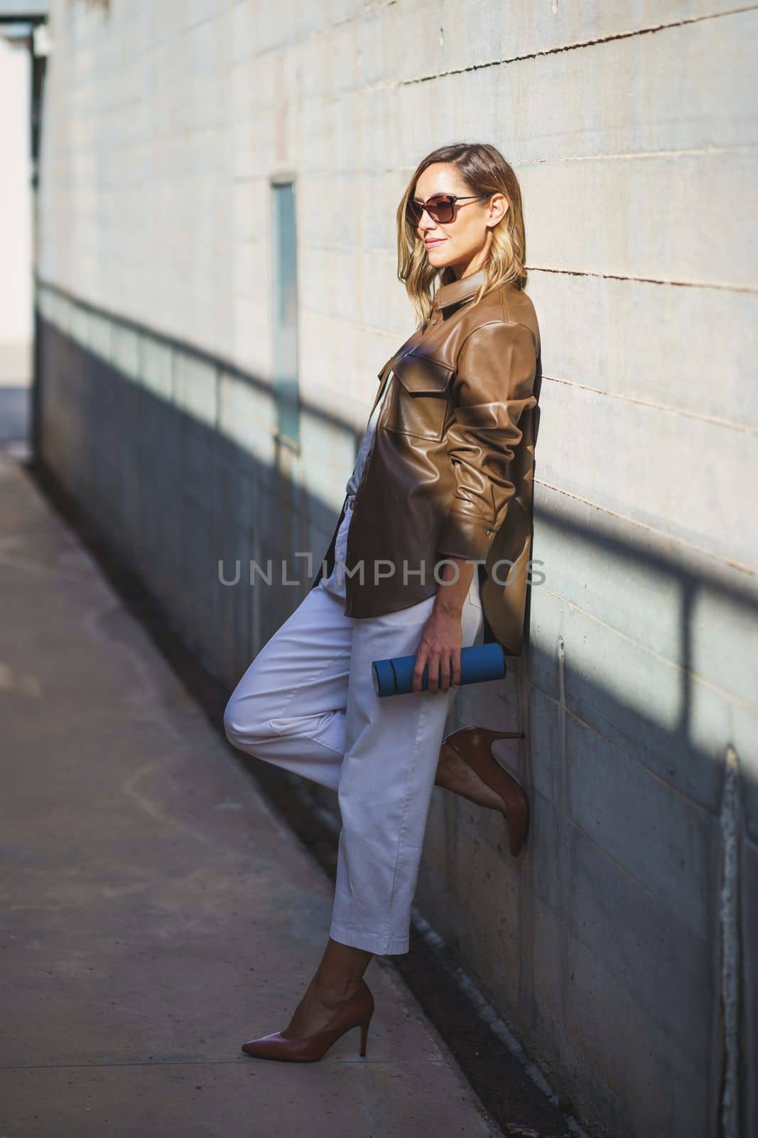 Stylish female leaning on sunlit wall by javiindy