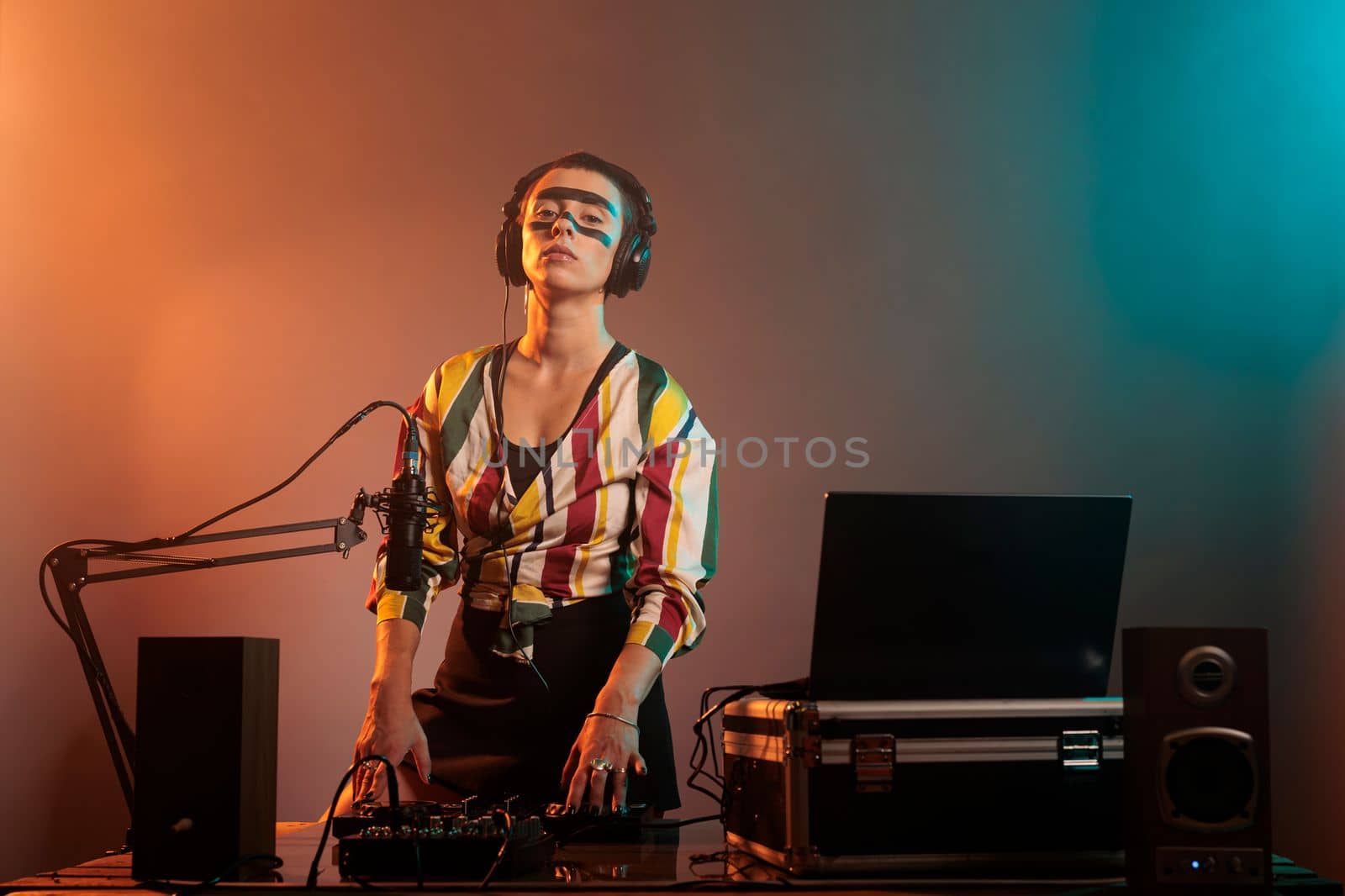 Cheerful musical artist working as dj with turntables, mixing techno music with bass and audio equipment. DJ woman playing songs at mixer, standing over colorful background with smoke.