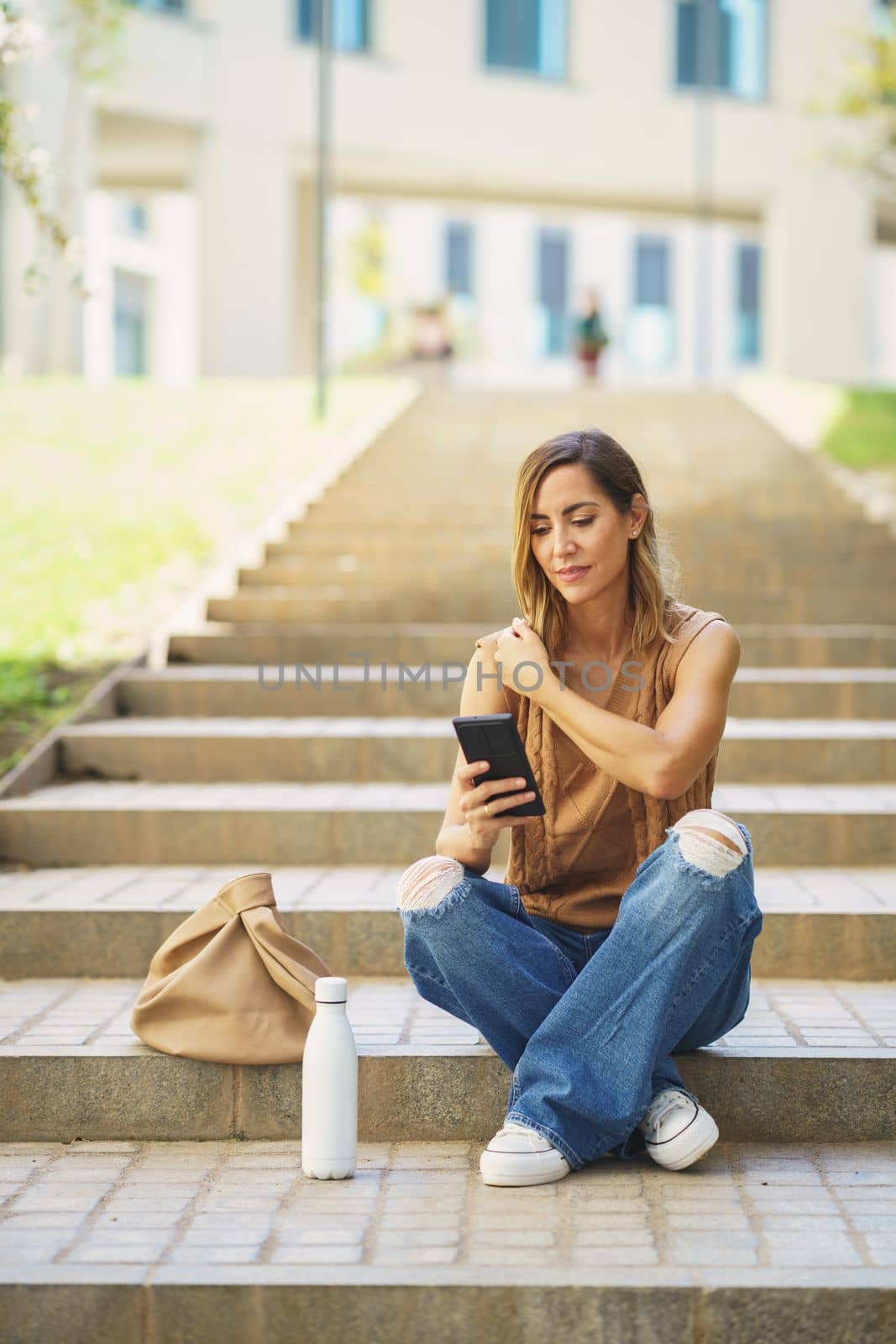 Female with smartphone sitting on stairs by javiindy