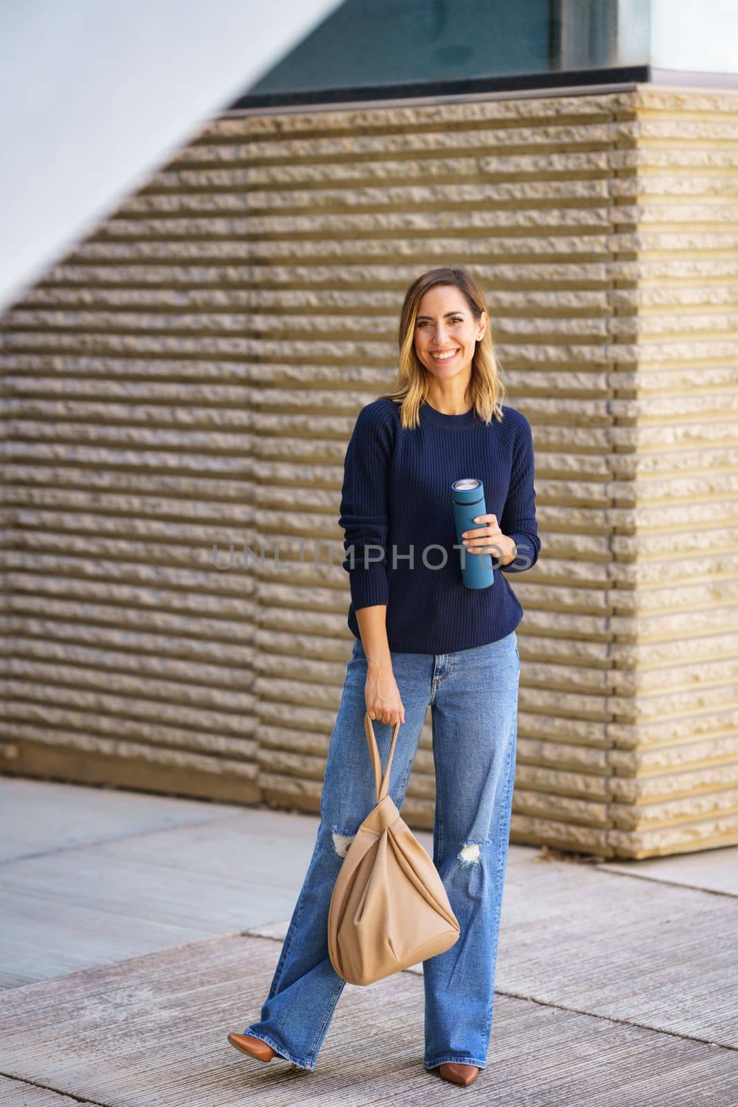 Cheerful woman with thermos and bag on street by javiindy