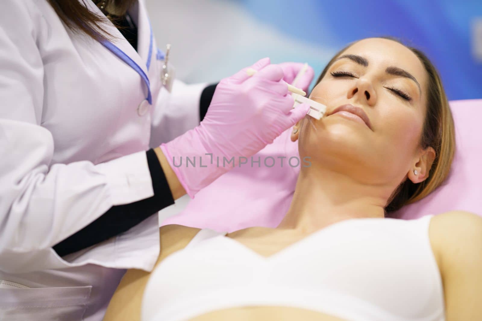 Doctor painting the area of a middle-aged woman's face where the PDO suture treatment threads will be injected.