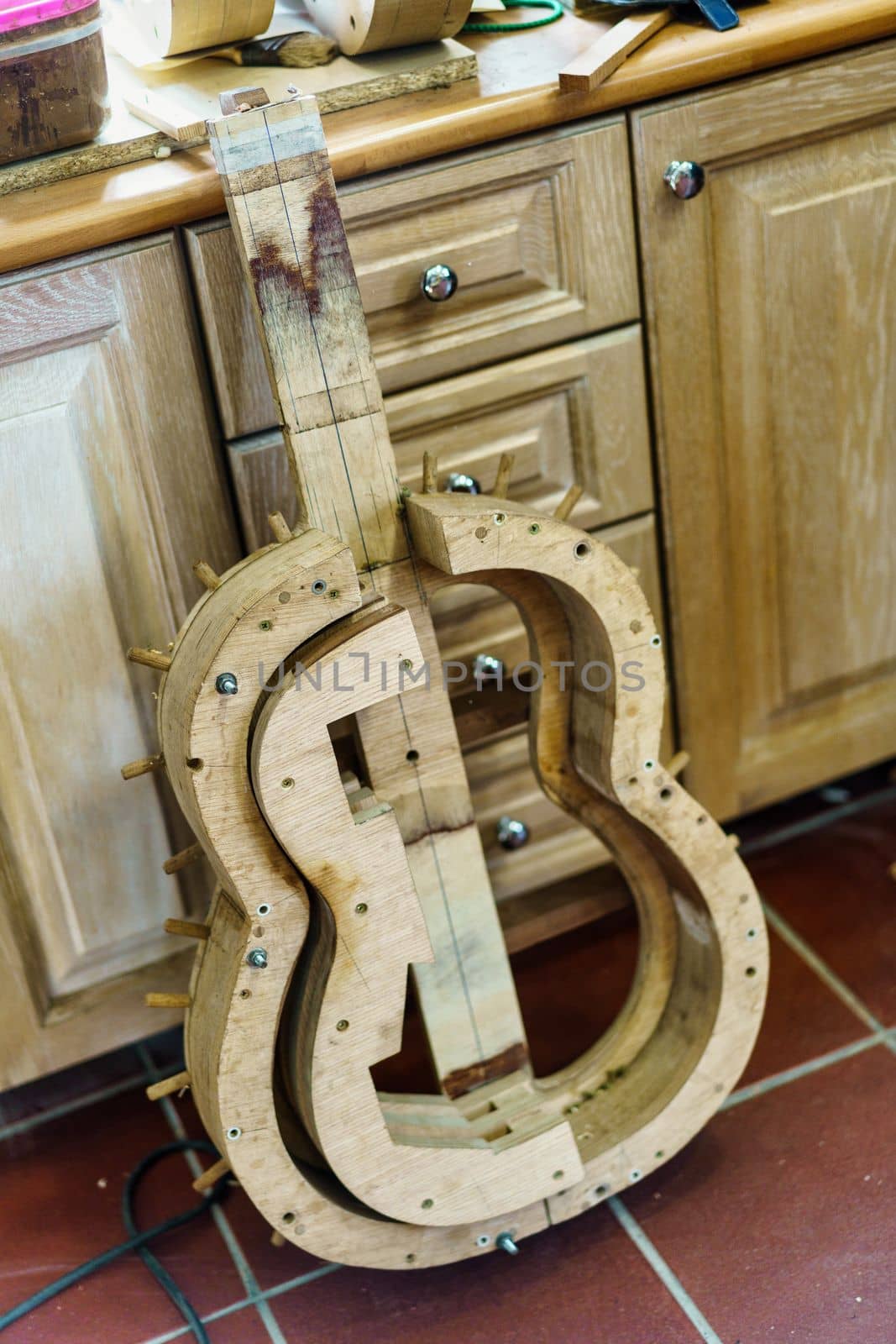 From above wooden mould for making Spanish flamenco guitar placed on tiled wall near cabinets in professional luthier workshop.