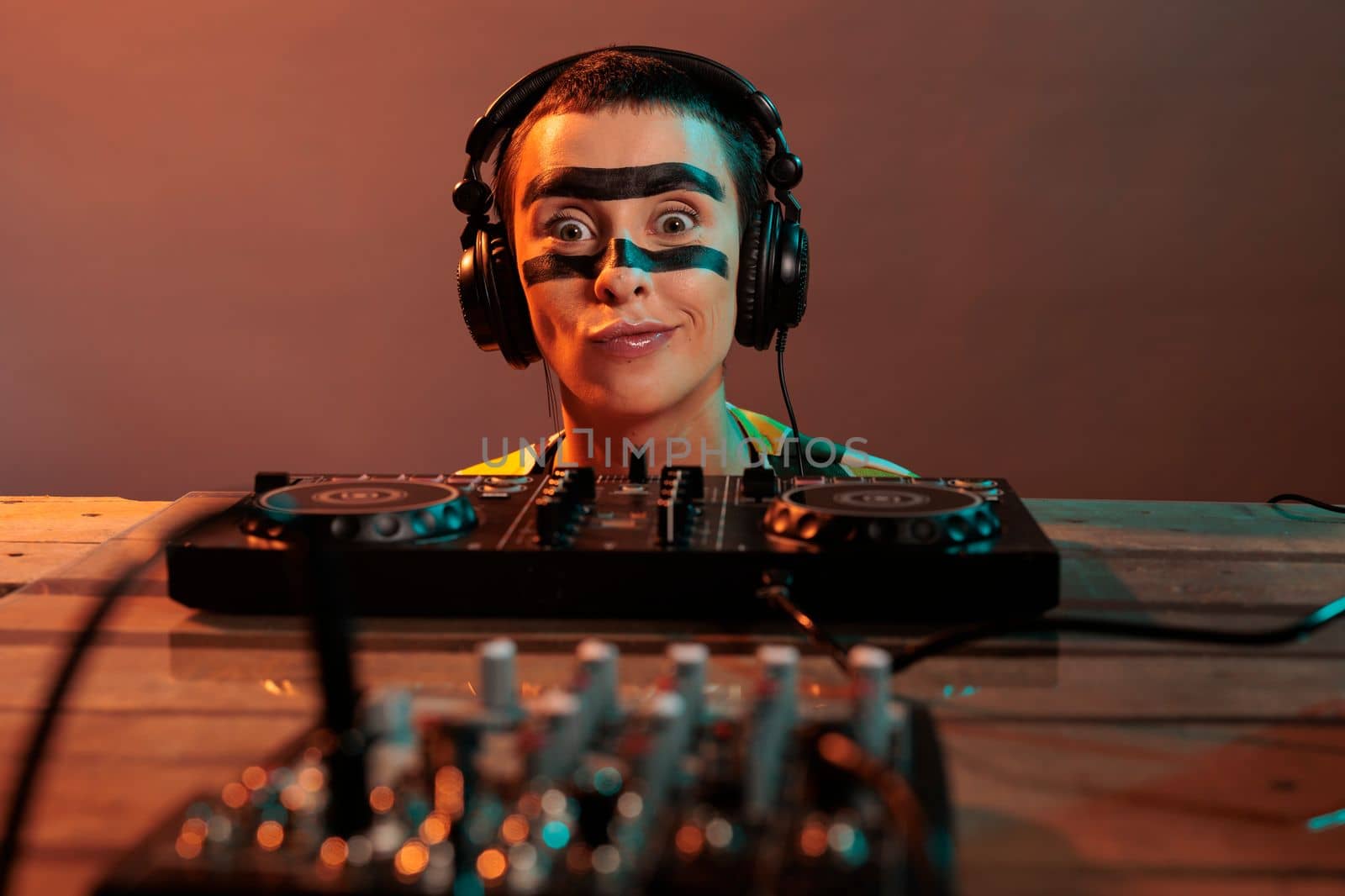 Young performer acting funky looking at mixer, being focused on control buttons at dj turntables over background. Looking closely at audio equipment to mix techno music, stereo instrument.