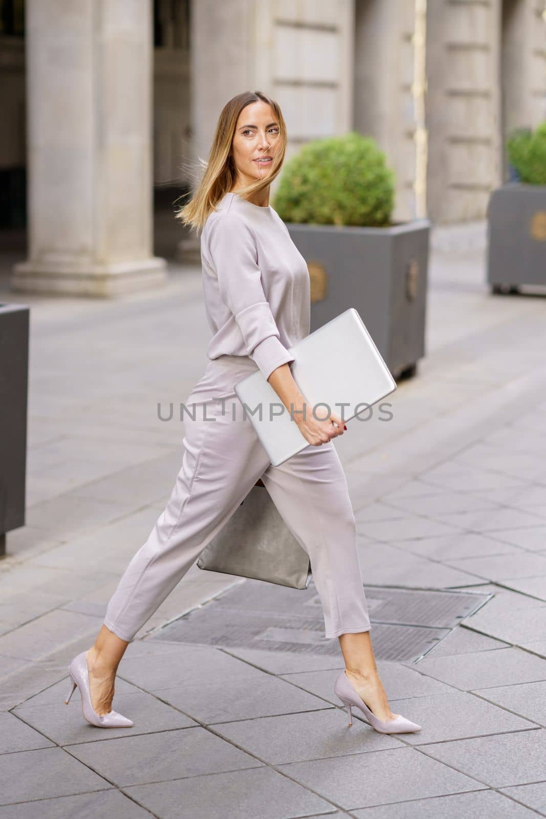 Self assured female manager with laptop crossing street near building by javiindy