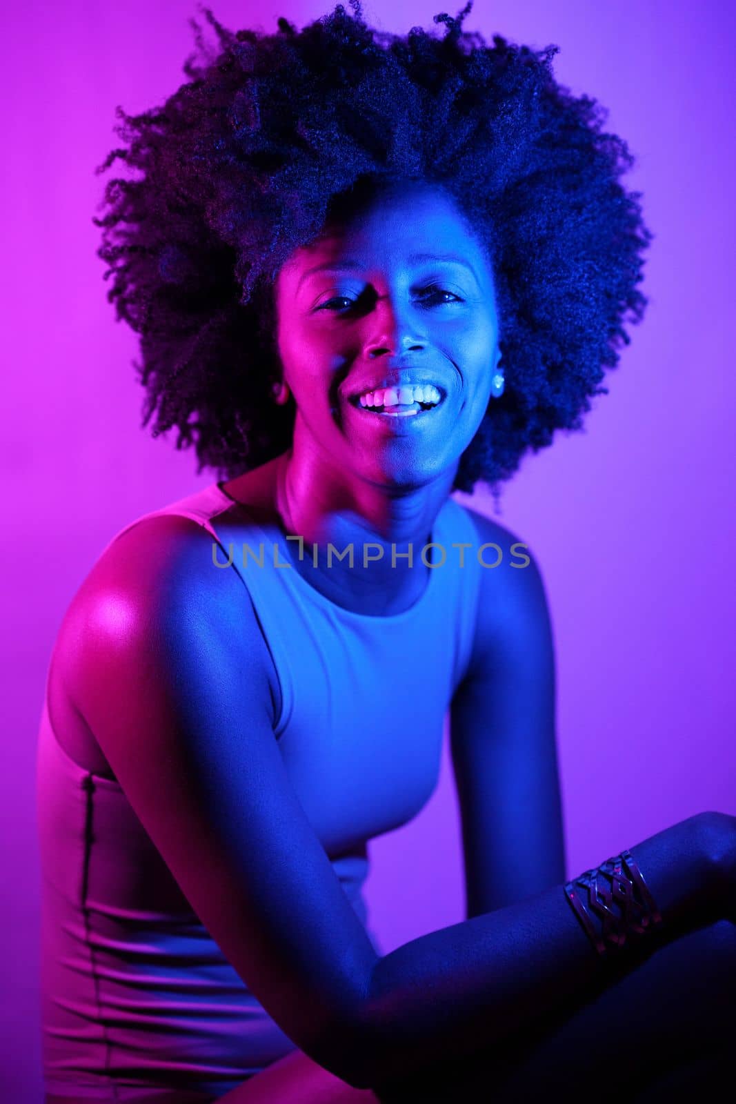 Happy African American woman with curly hair smiling and looking at camera under violet neon light