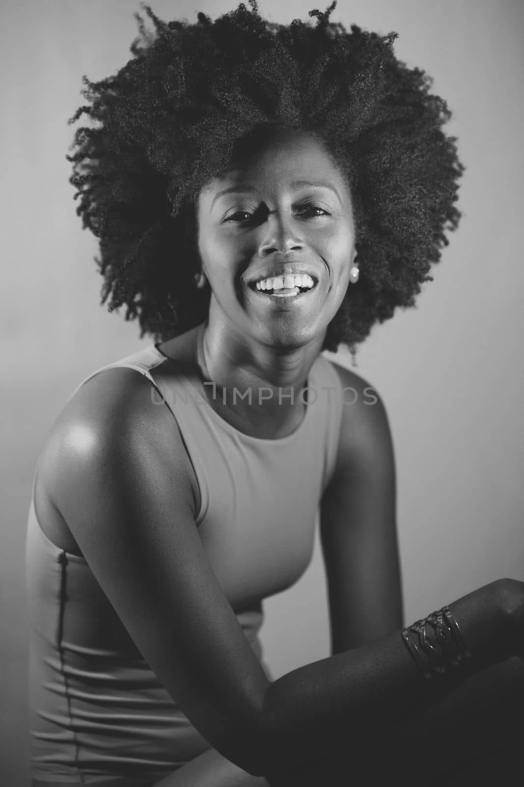 Happy African American woman with curly hair smiling and looking at camera under violet neon light. Black and white photograph.