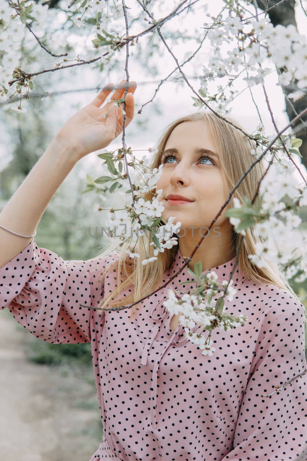 Blonde girl on a spring walk in the garden with cherry blossoms. Female portrait, close-up. A girl in a pink polka dot dress