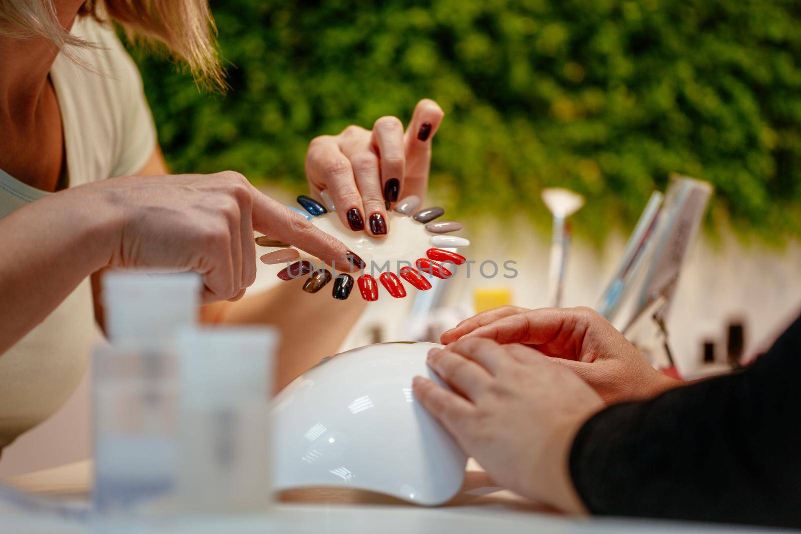 Close-up of a beautician and female clients hands holding samples and choosing colours nails at the beauty salon.