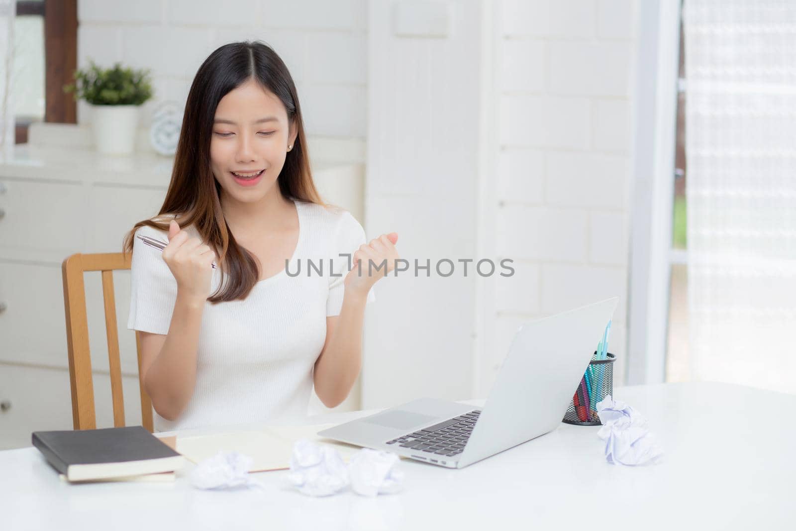 Young asian woman confident working at home with laptop computer and thinking idea for planning, freelance happy girl excited and success using notebook thoughtful and writing, business concept.