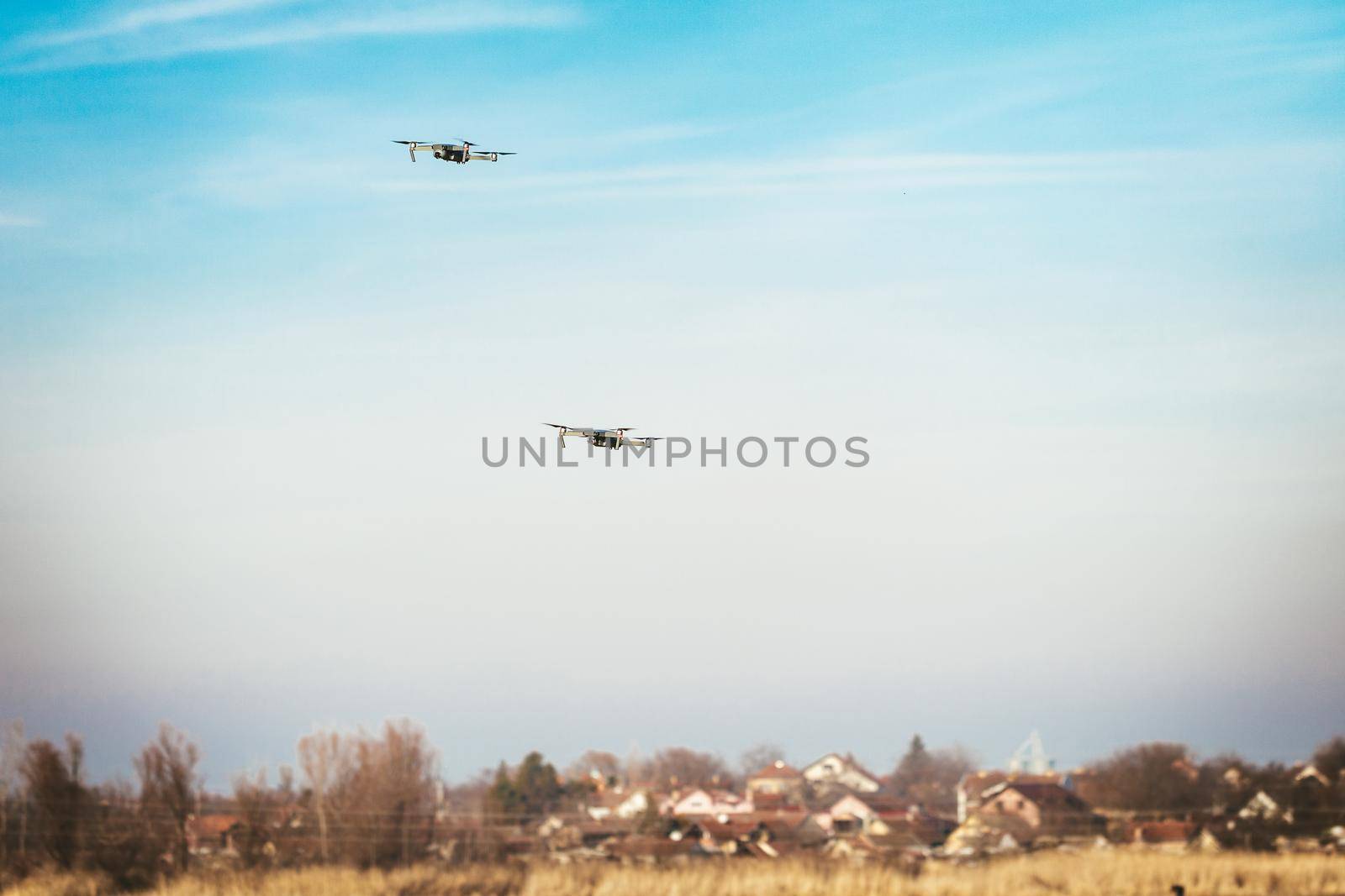 Two drones flying in the sky over the village, for racing and shooting video. Copy space.