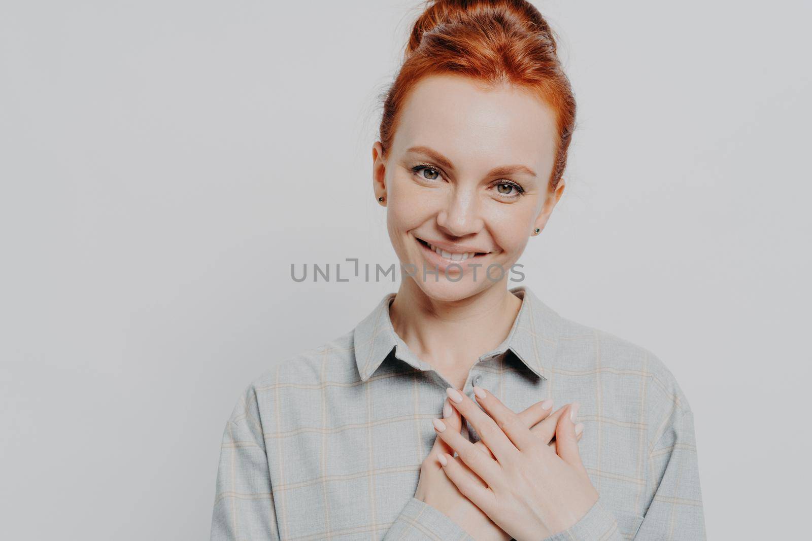 Headshot of young grateful ginger holding hands on chest, feeling love and appreciation, lovely red haired caucasian female thanking while posing isolated on grey studio background. Body language