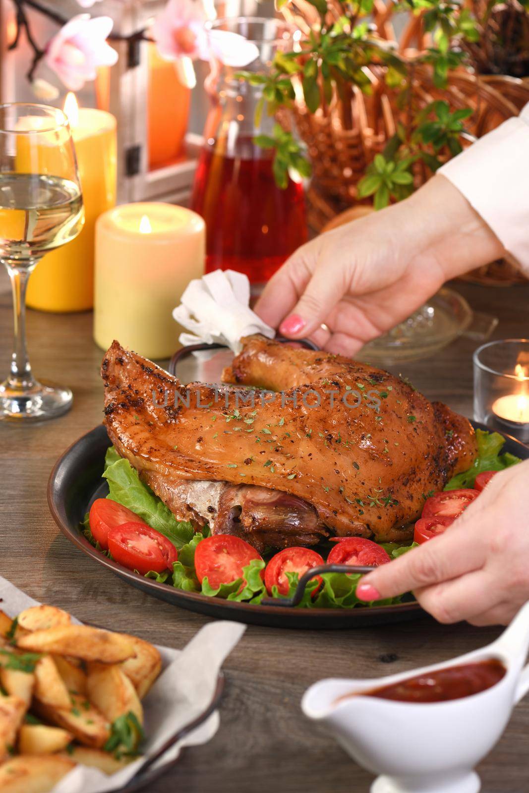 Woman serving baked drumstick turkey on a tray of vegetables on the dining table.. Happy Thanksgiving.