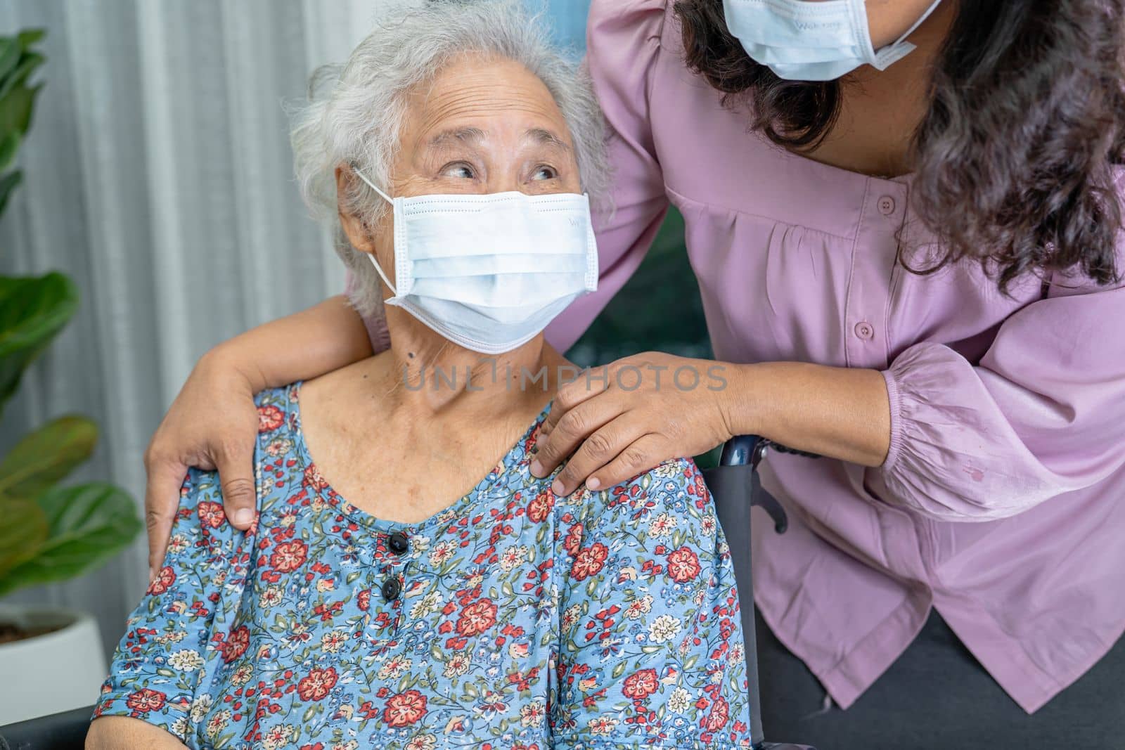 Caregiver help Asian senior or elderly old lady woman sitting on wheelchair and wearing a face mask for protect safety infection Covid 19 Coronavirus.