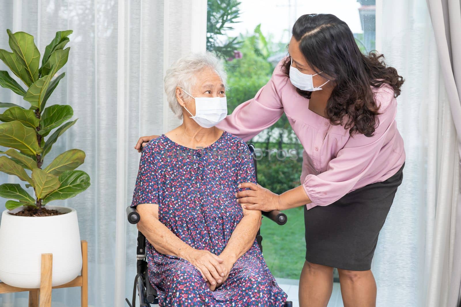 Caregiver help Asian senior or elderly old lady woman sitting on wheelchair and wearing a face mask for protect safety infection Covid19 Coronavirus. by pamai