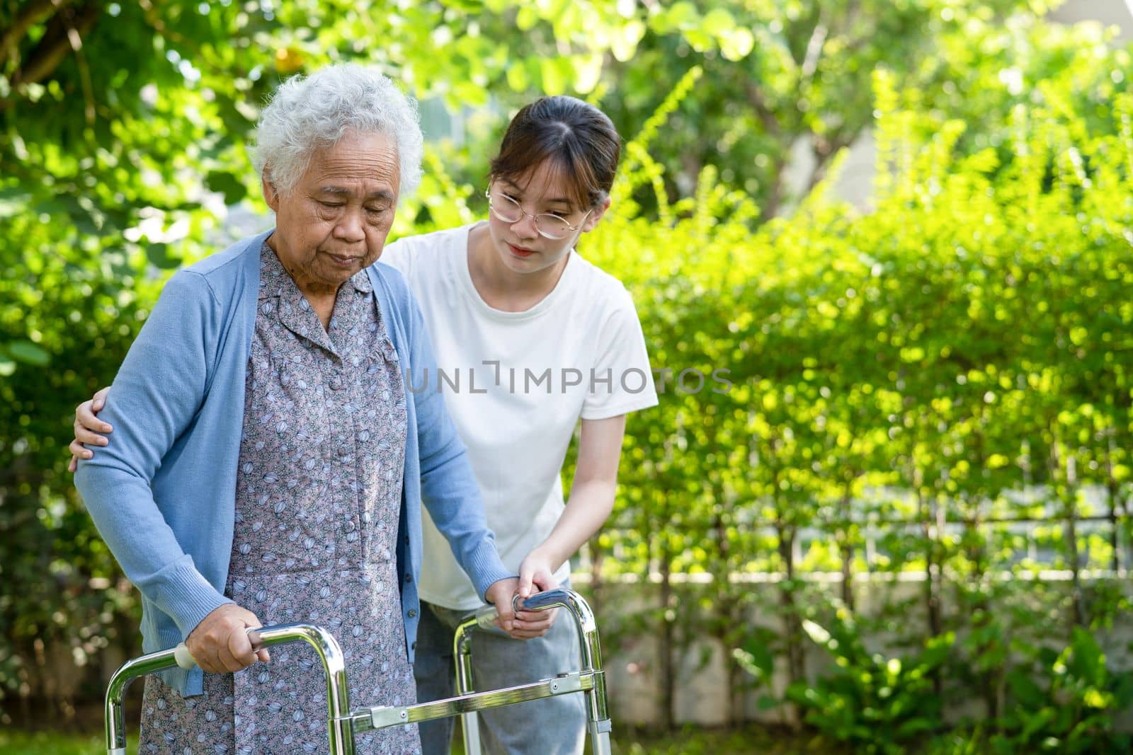 Caregiver help and care Asian senior or elderly old lady woman use walker with strong health while walking at park in happy fresh holiday. by pamai