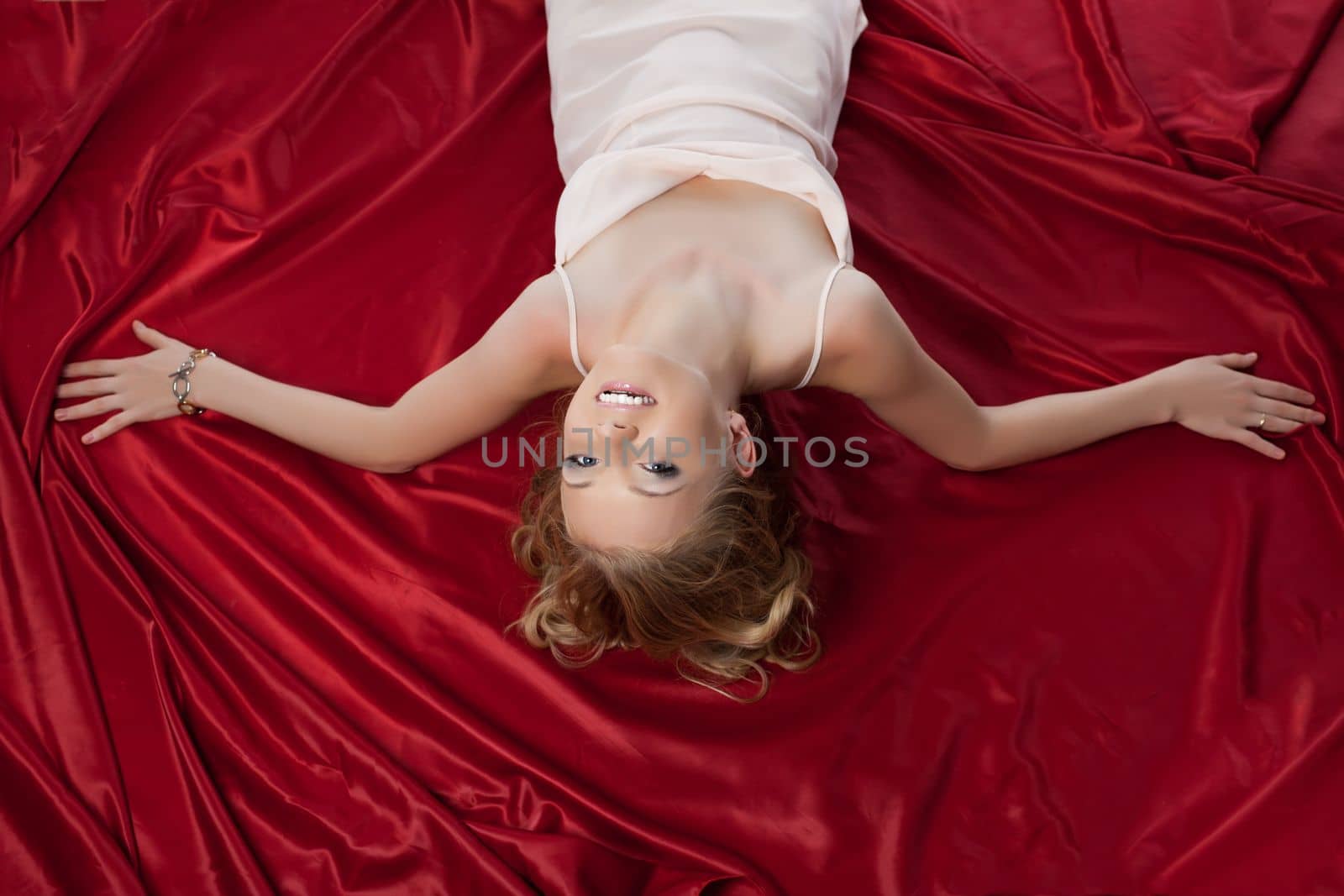 Beautiful blonde woman lying on red sheet