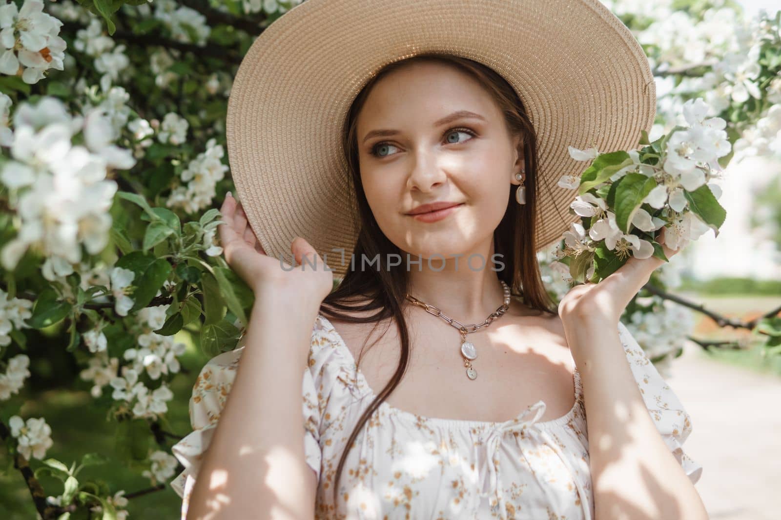 An attractive long-haired woman walks in the spring in the park of blooming apple trees. Spring portrait of a woman