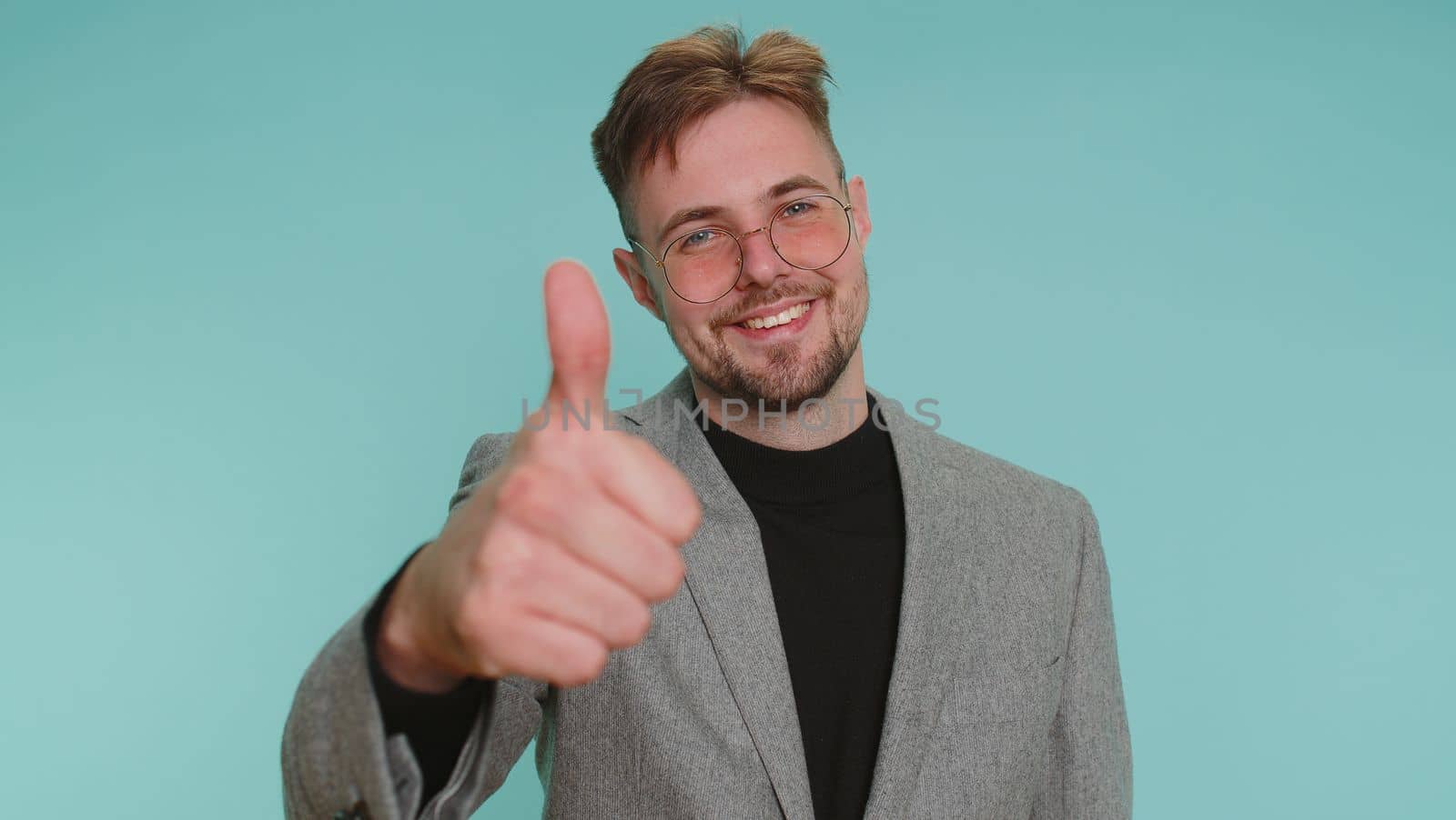 Like. Bearded adult business man in jacket suit raises thumbs up agrees with something or gives positive reply recommends advertisement likes good. Young guy isolated alone on blue studio background