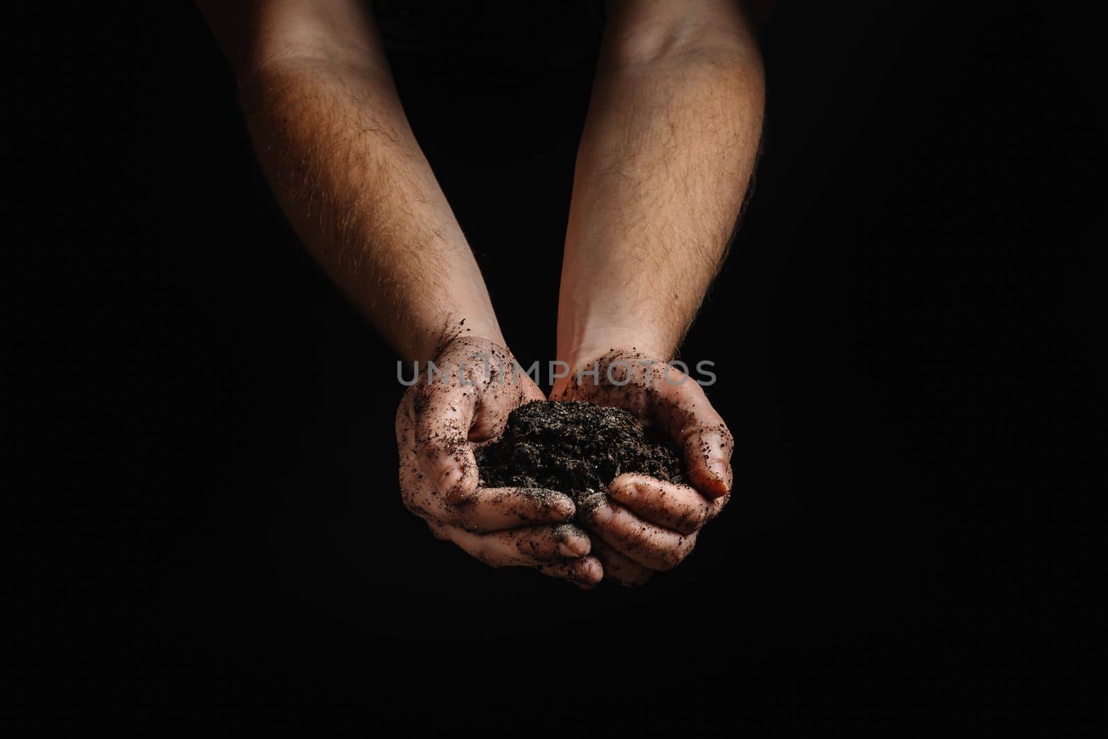 Dirty men's hands holding dark, moist soil. Agriculture, organic gardening, planting or the concept of ecology. Environment, Earth Day. Banner. Top view. Copy space