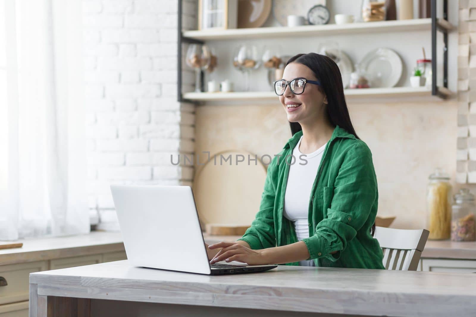 A young woman is working at home in the kitchen on a laptop.