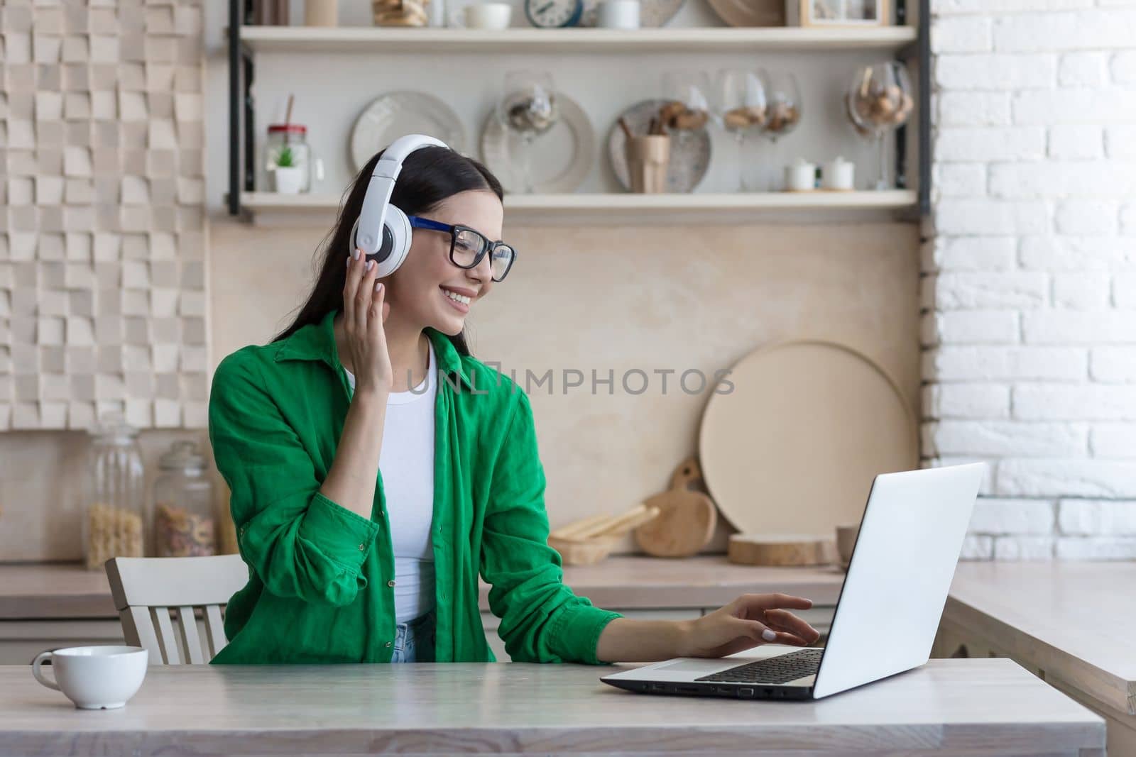 Young beautiful woman sitting in headphones at home at kitchen table and using laptop, Watch online webinar, movie, study.