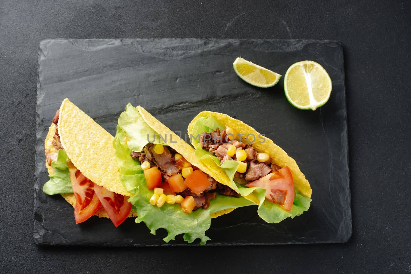 Mexican tacos with beef, vegetables and salsa. Tacos al pastor on a wooden board on a black background. Top view with copy space.
