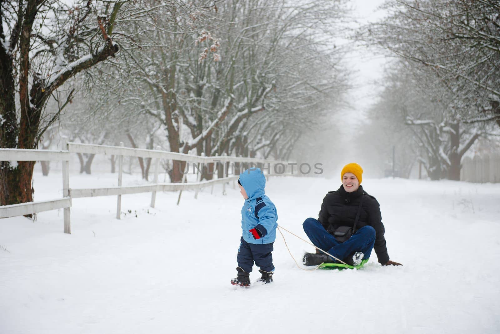 The son rides his father on a sled. Funny moments in winter. Activities in the cold season. Family spending free time together