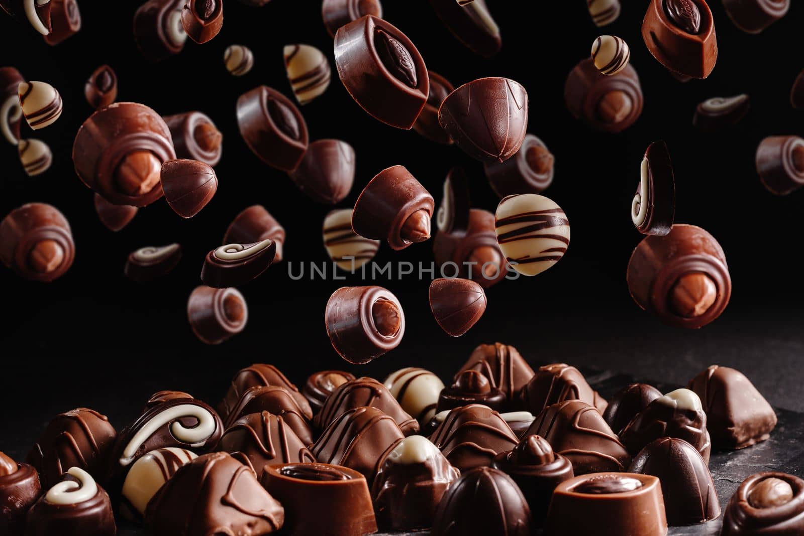 chocolate candies with various fillings, sweet food background. Levitation or flight of sweet brown chocolates or confit on a dark black background by gulyaevstudio