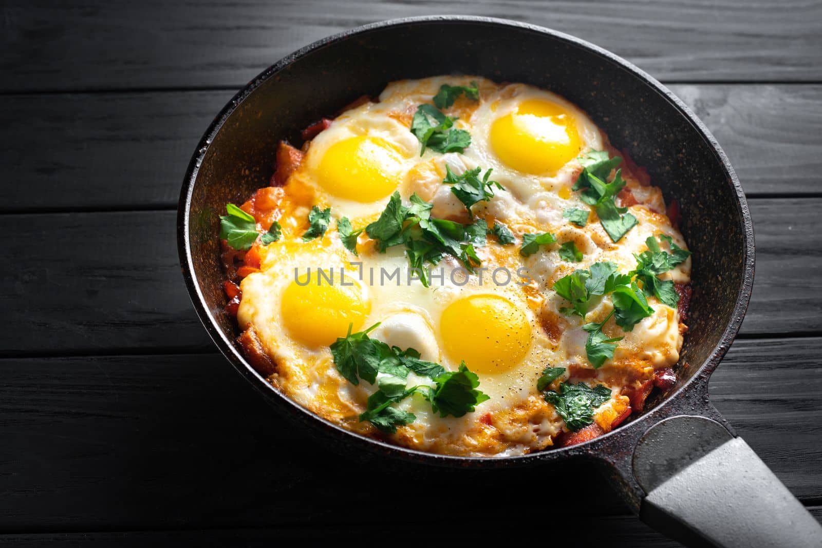 Pan of fried eggs and tomatoes on a dark table surface, top view. Egg breakfast. Eggs for breakfast by gulyaevstudio