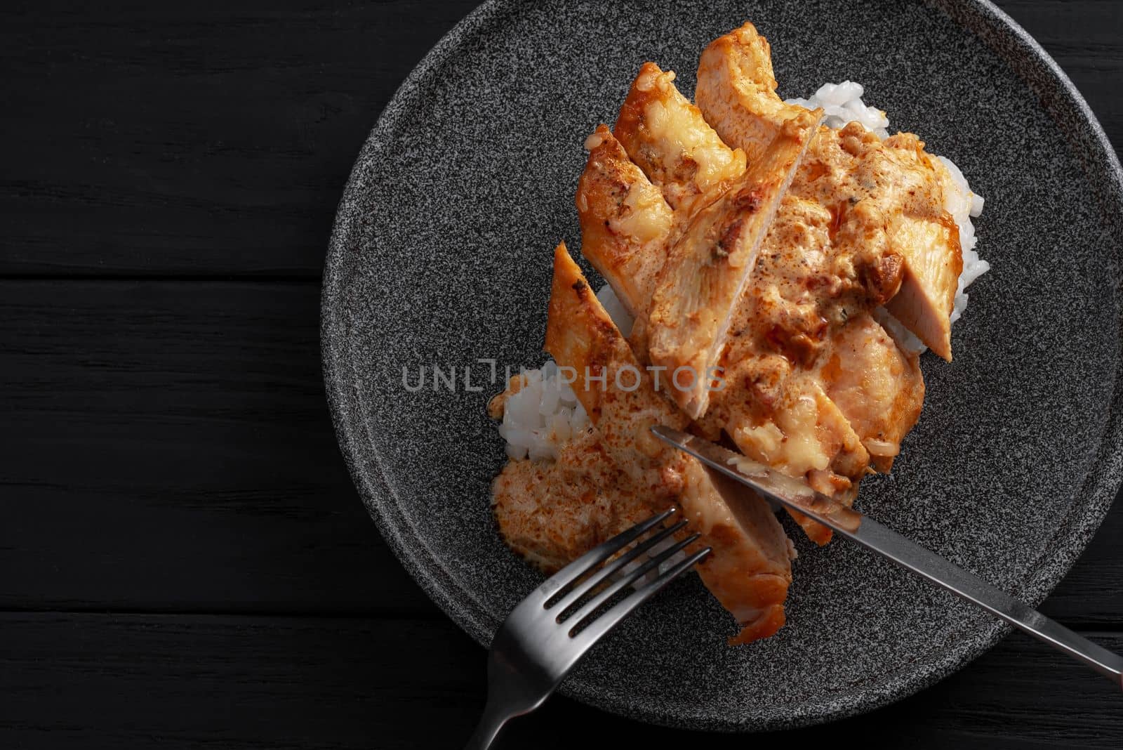 A man is eating an Indian dish. Hands holding knife and fork. Indian chicken with butter and basmati rice in a plate. .Black background. Place for text. Chicken in oil, a traditional Indian dish. Top view. Chicken tikka masala. Indian Cuisine.