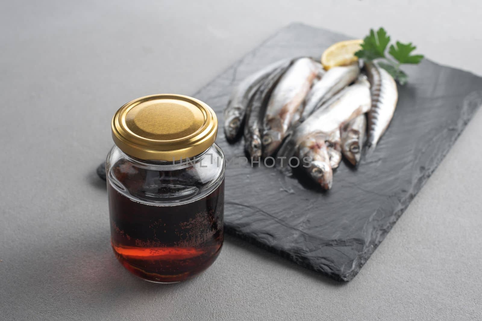 Garum is a fermented fish sauce. Prepared by fermentation from fish, salted garum sauce in a bottle on a gray background. Garum fish sauce made from anchovies on the grey background.