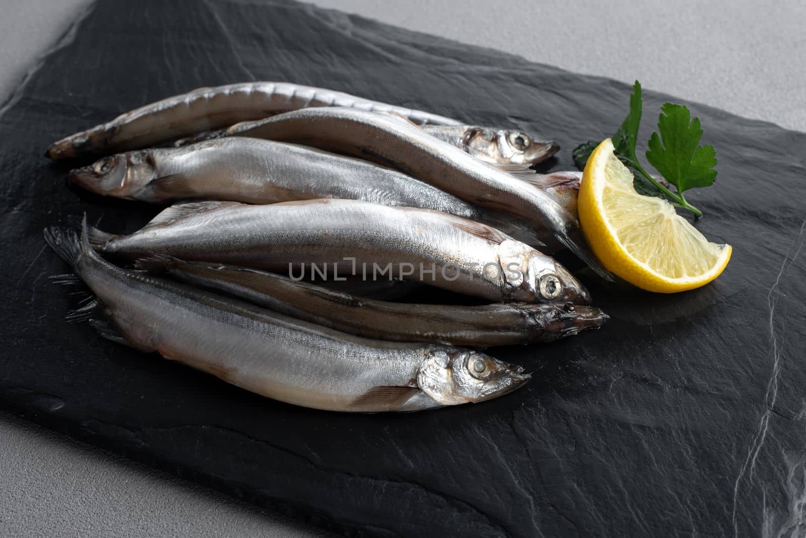 Raw fresh fish capelin with lemon. Gray background. Top view. by gulyaevstudio