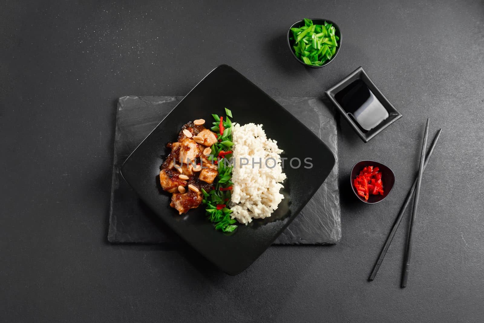 Kung Pao chicken or Gong Bao Ji Ding on a dark concrete background. Sichuan kung pao is a Chinese dish with chicken meat, chili peppers, peanuts, sauces, and onions. Copy place. Top view by gulyaevstudio
