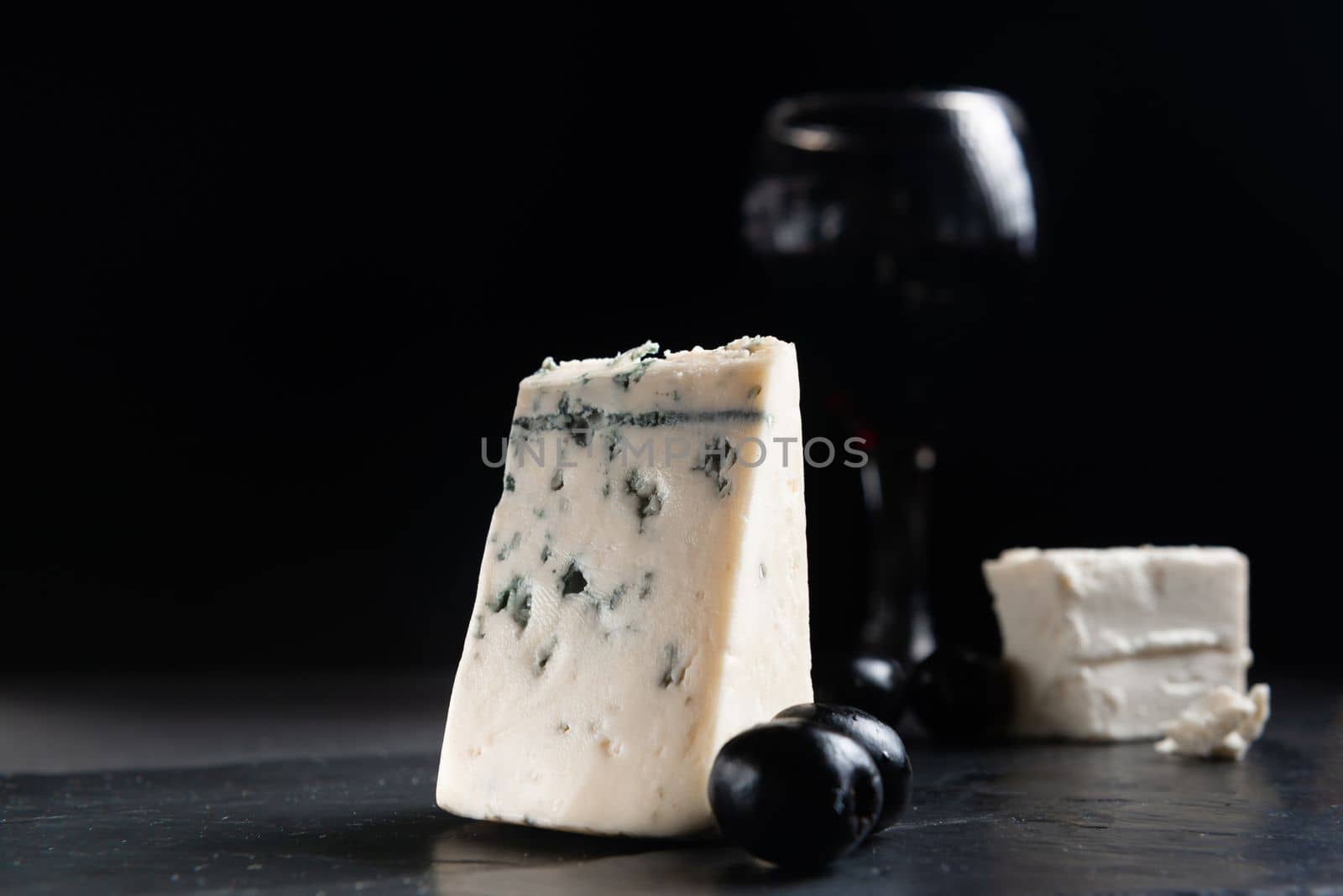 French Roquefort cheese with olives on a dark background. Moldy cheese with olives. Blue cheese on black background.
