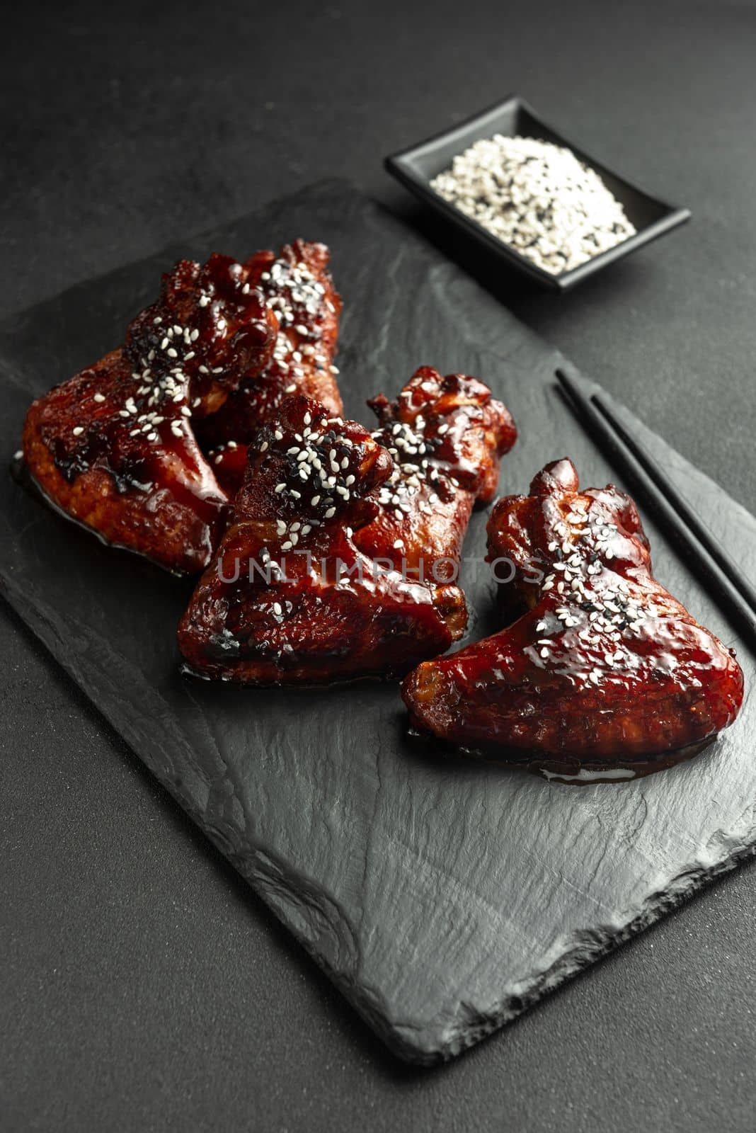 Asian-style chicken wings in sour sweet sauce on a plate on a dark stone background with space to copy. Top view, flat plan. Sticky honey-soy chicken wings on plate over dark stone background. Top view, flat lay, close up