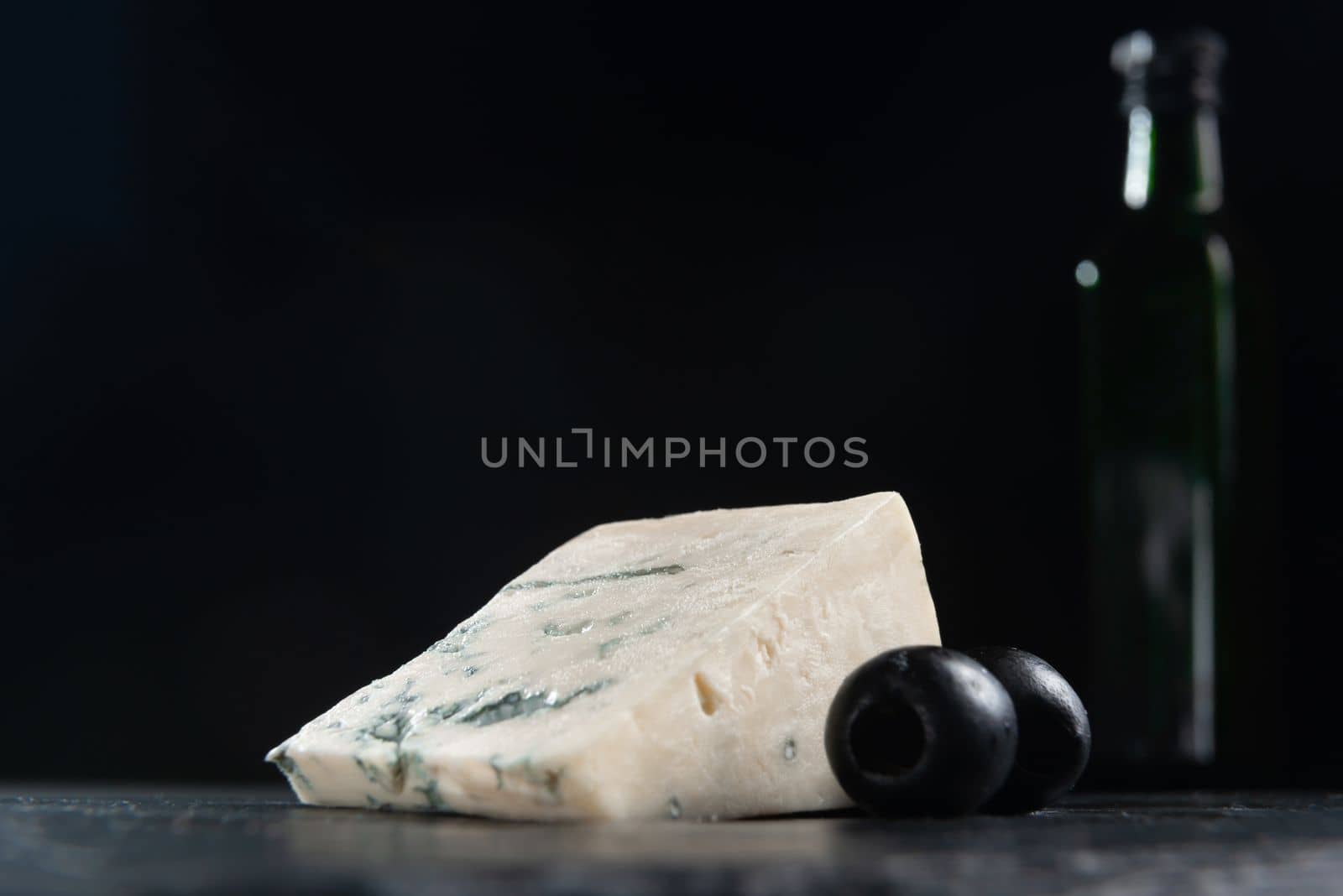 French cheese, roquefort with olives on plate, closeup. French Roquefort cheese with olives on a dark background. Moldy cheese with olives. Blue cheese on black background by gulyaevstudio
