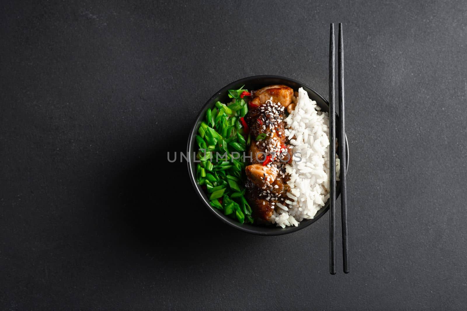 Asian food. Kung Pao on a gray background in a black plate top view. Kung Pao Chicken or Gong Bao Ji Ding at dark slate background. Sichuan Kung Pao is chinese cuisine dish with chicken meat, chilli peppers, peanuts, sauces and onion. Copy space. Top view.