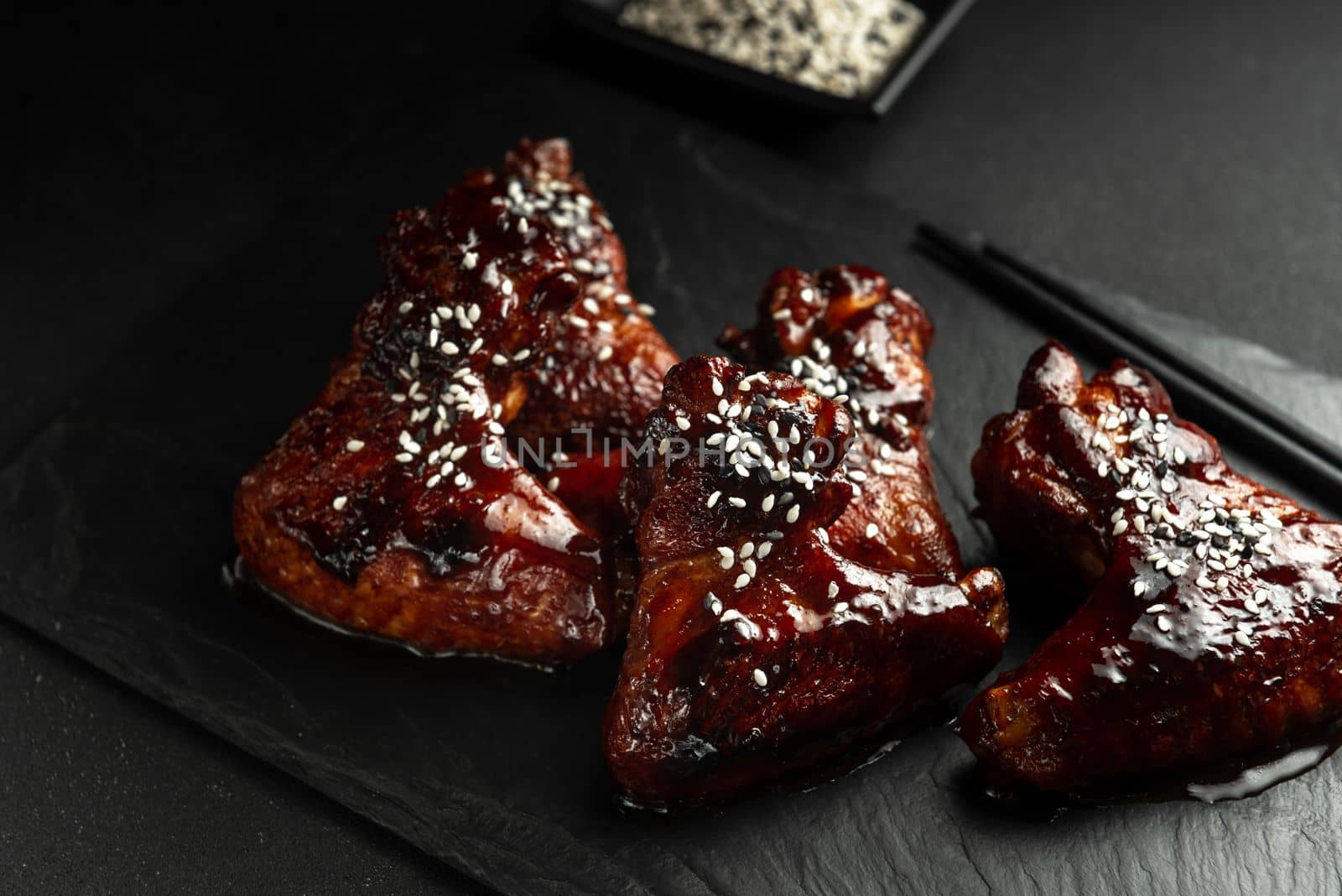 Asian-style chicken wings in sour sweet sauce on a plate on a dark stone background with space to copy. Top view, flat plan.