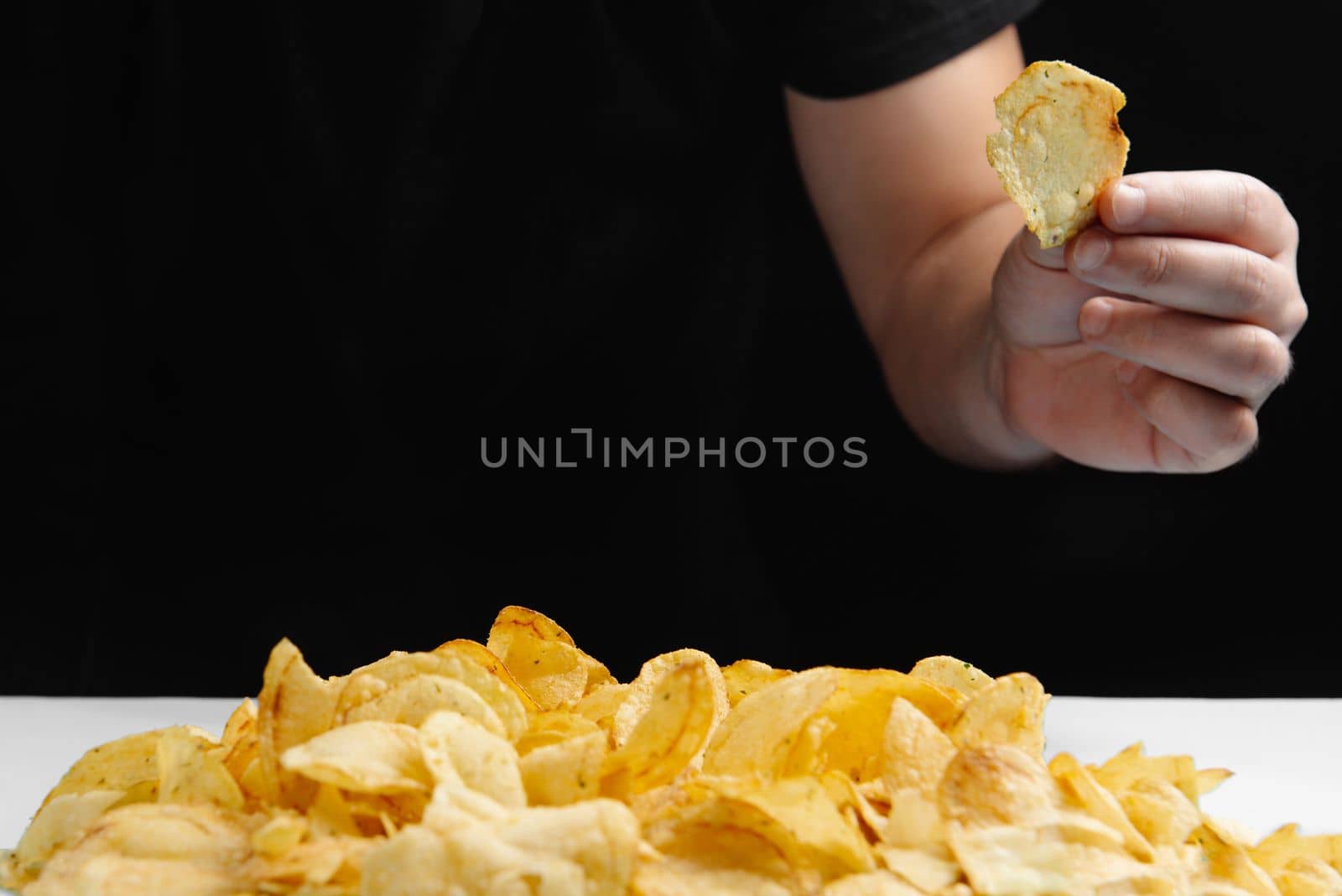The man is eating junk food, chips on a dark background. Harmful food. Fried food is bad for your health. Healthy lifestyle, proper nutrition, ban on unhealthy foods. The ban on chips. Stop banned foods