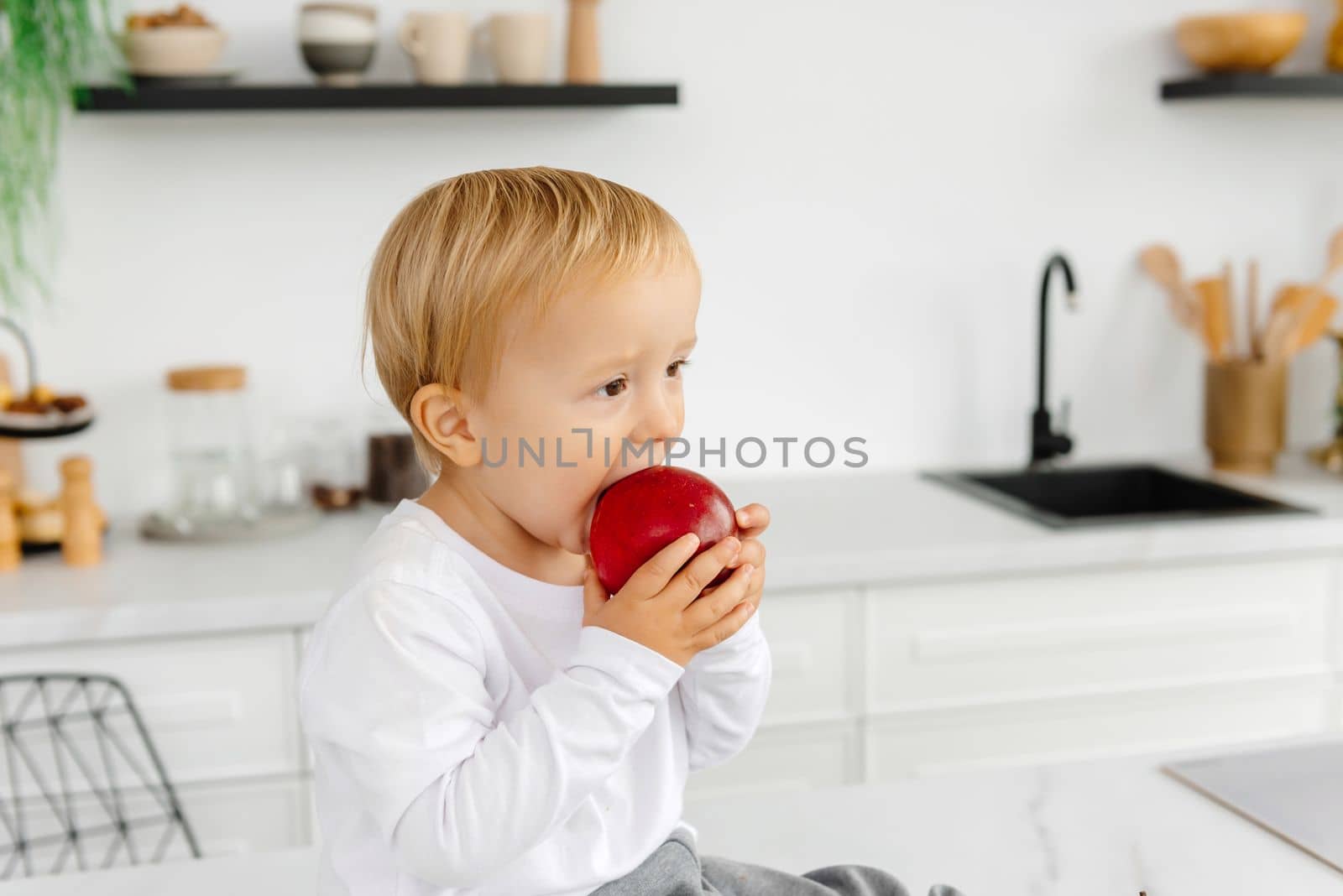 The child eats an apple for breakfast sitting in the kitchen. Healthy eating for the whole family by gulyaevstudio