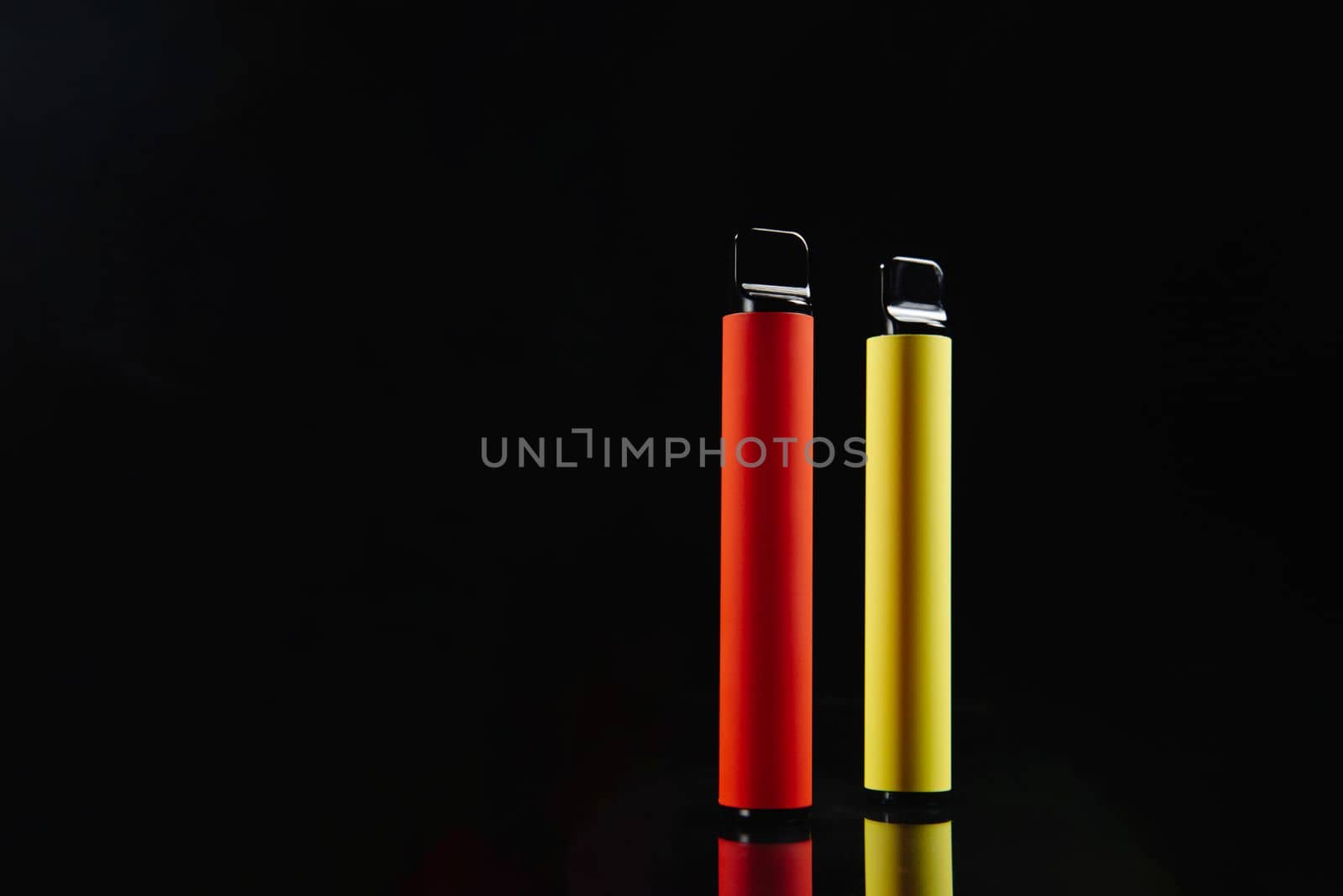Two disposable e-cigarettes on a dark background. Electronic vape, an alternative to smoking cigarettes. by gulyaevstudio
